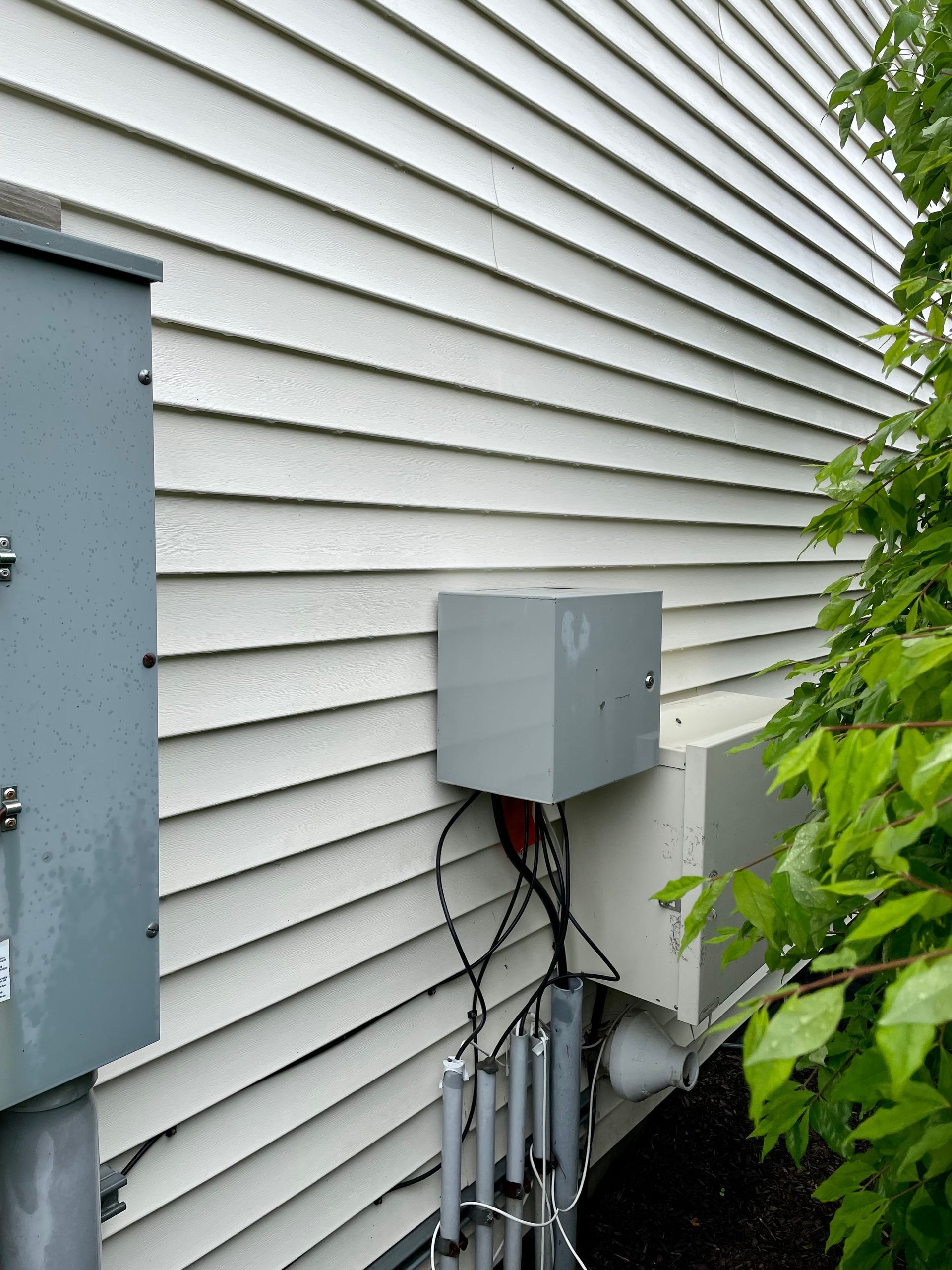 Gray electrical boxes and conduit attached to white siding on a building.