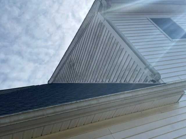 Close-up of a house exterior with white siding, a black roof, and a clear sky.