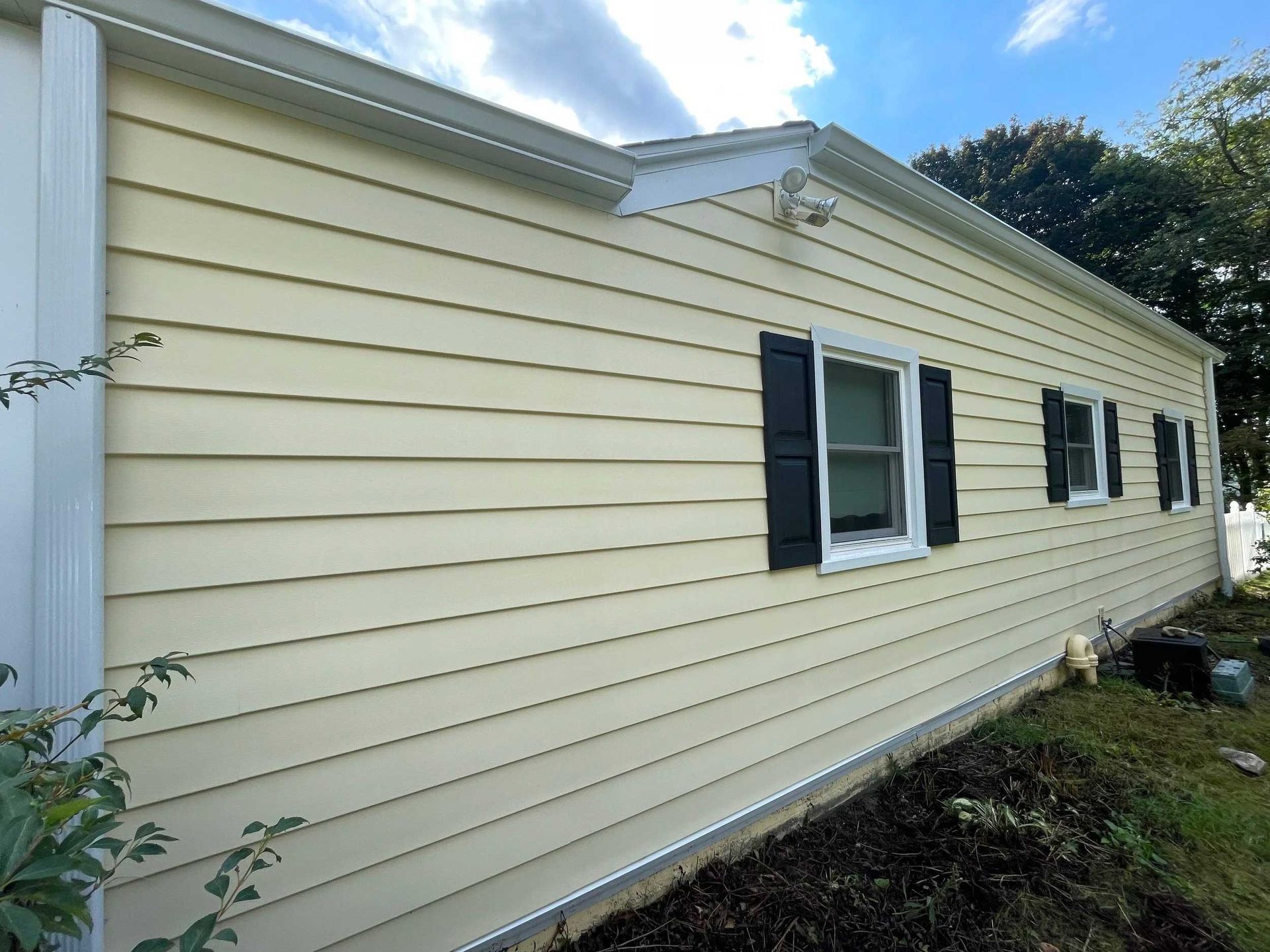 Yellow-sided house with black shutters on windows, white trim, and a blue sky in the background.