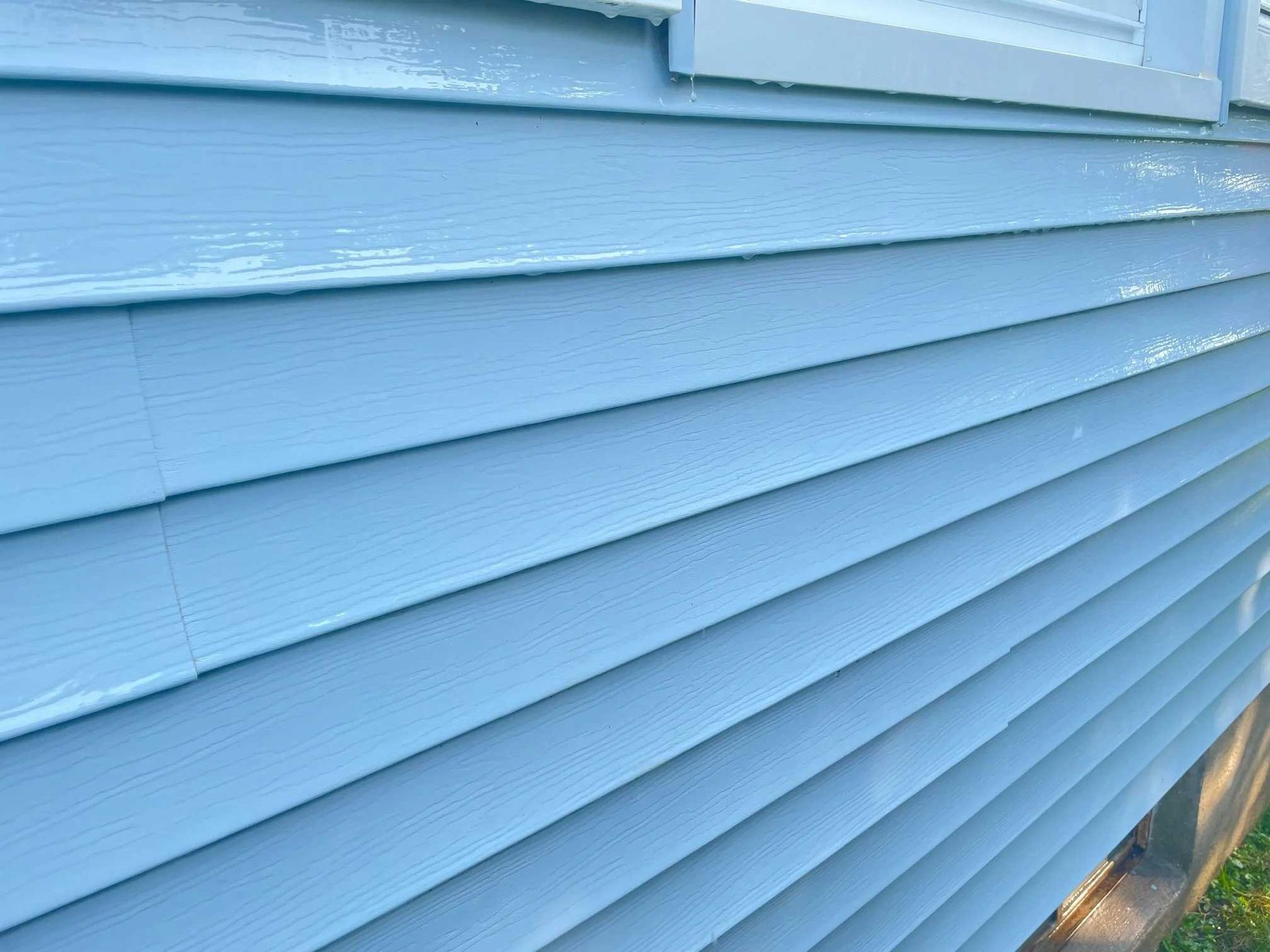 Light blue vinyl siding on a house exterior; some wet spots and a white window frame visible.