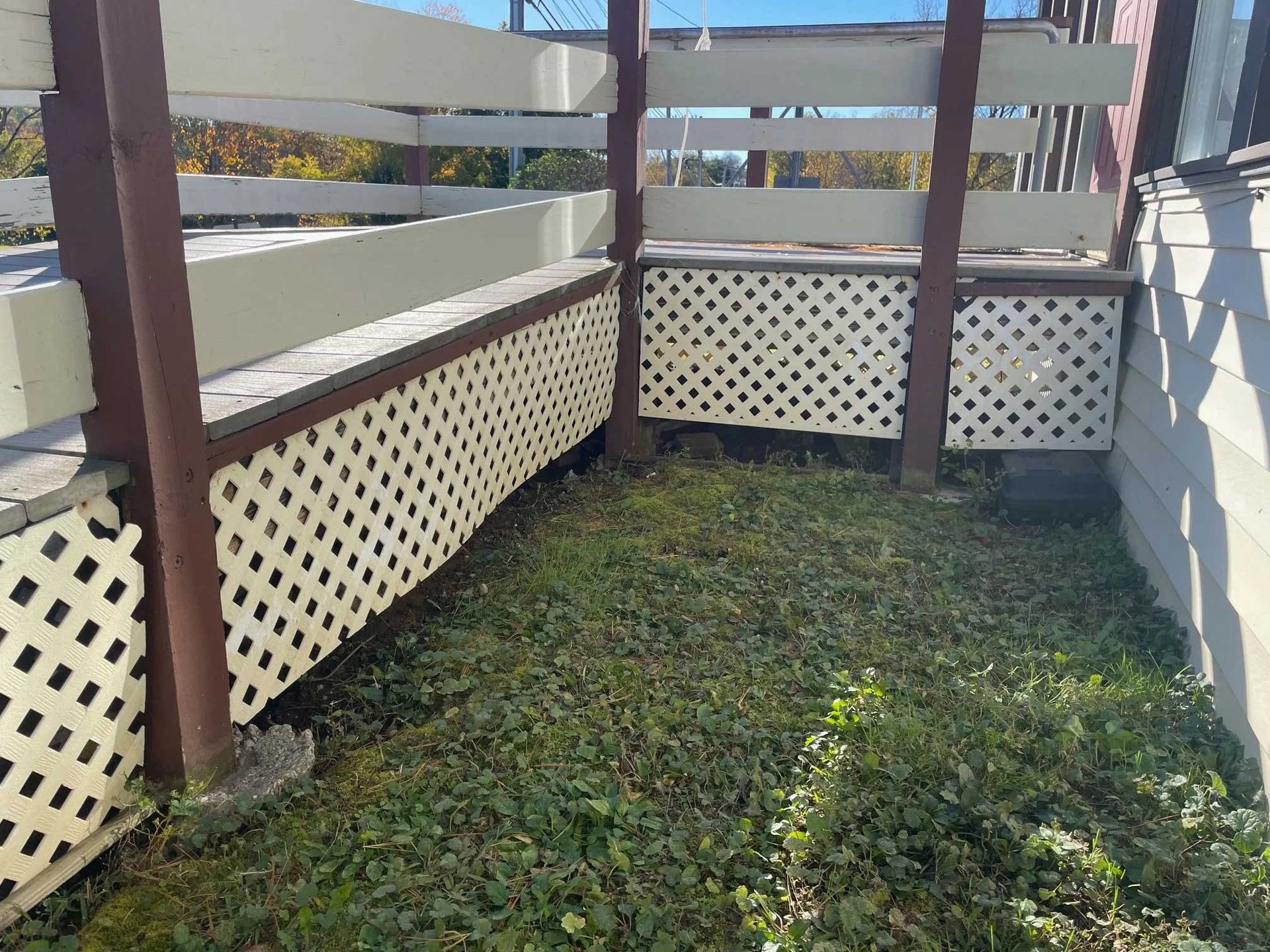Wooden deck with white lattice skirting and overgrown grass below.