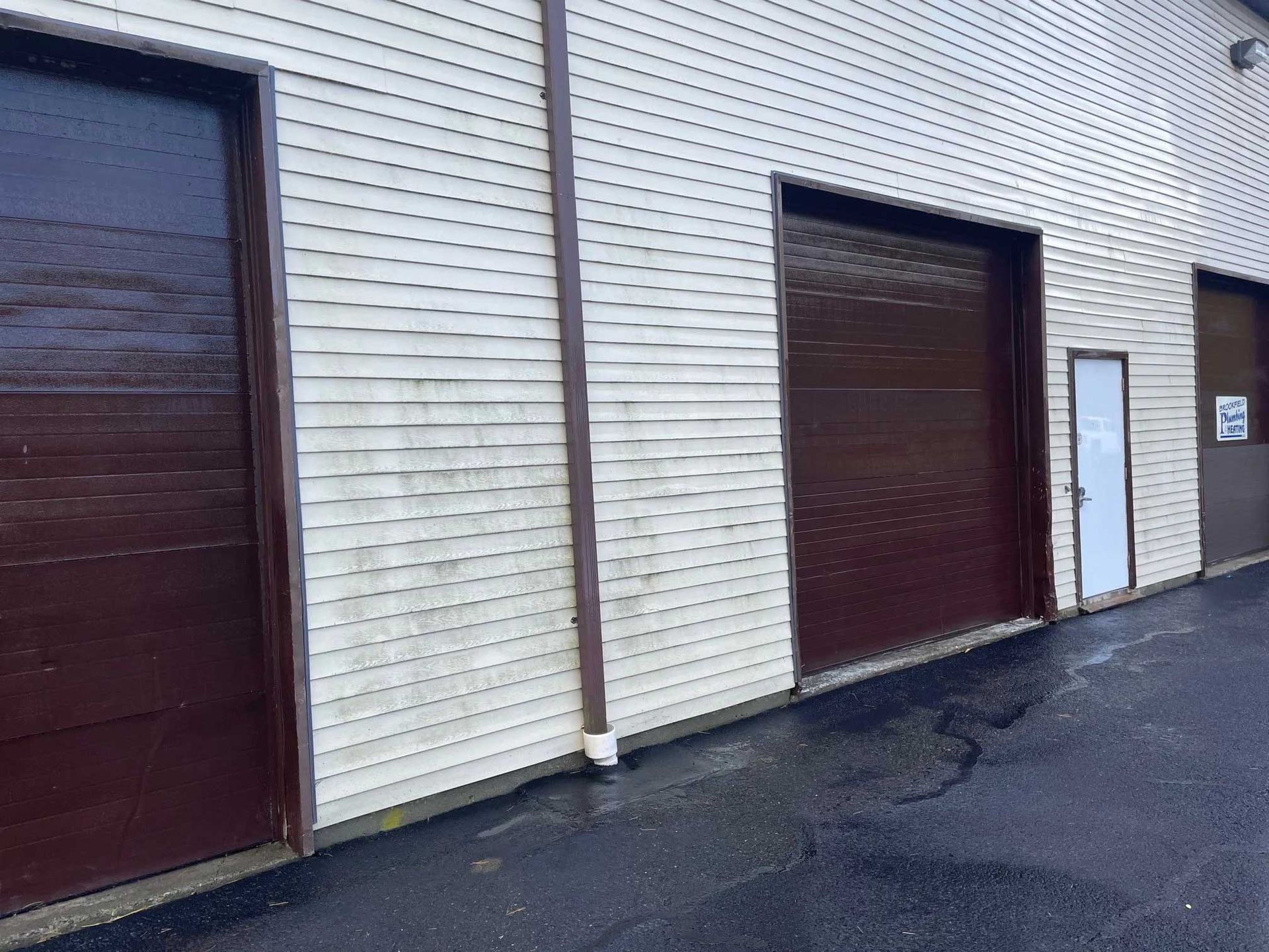 Brown garage doors and a small door on a light-colored building with dark asphalt.