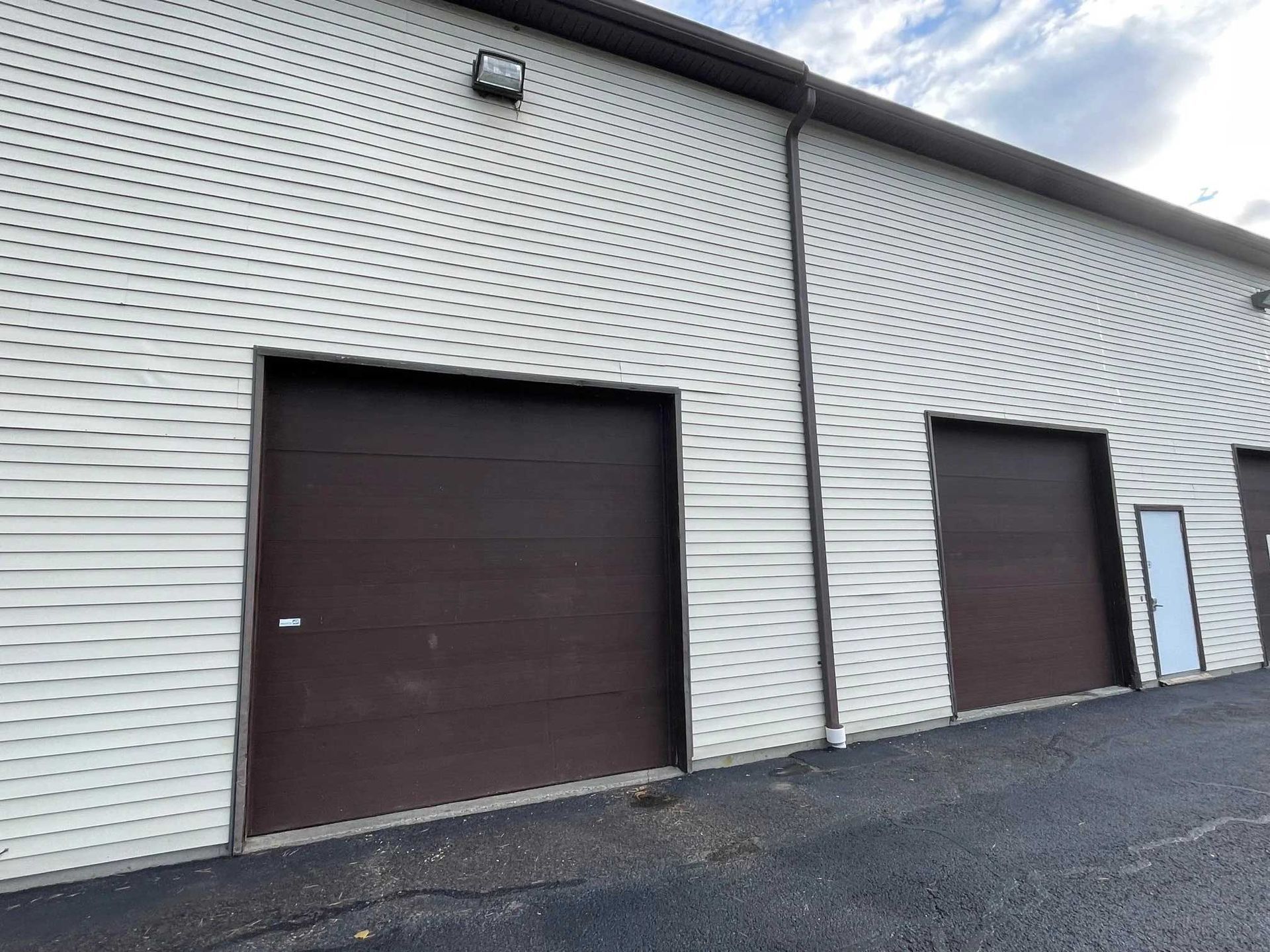 Exterior view of a commercial building with brown garage doors and white siding.