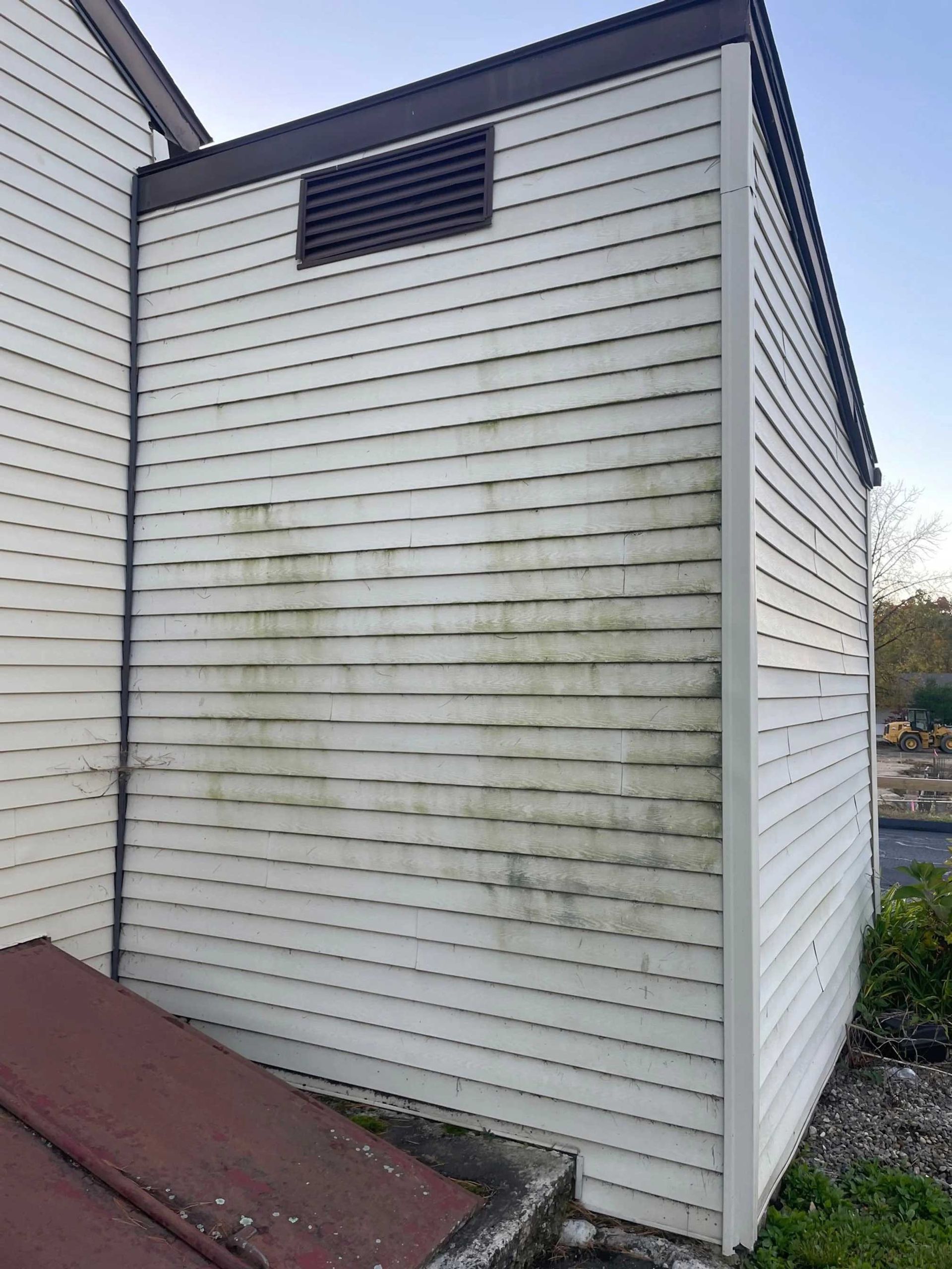 White siding on a building with green and black stains, vent, and brown trim.