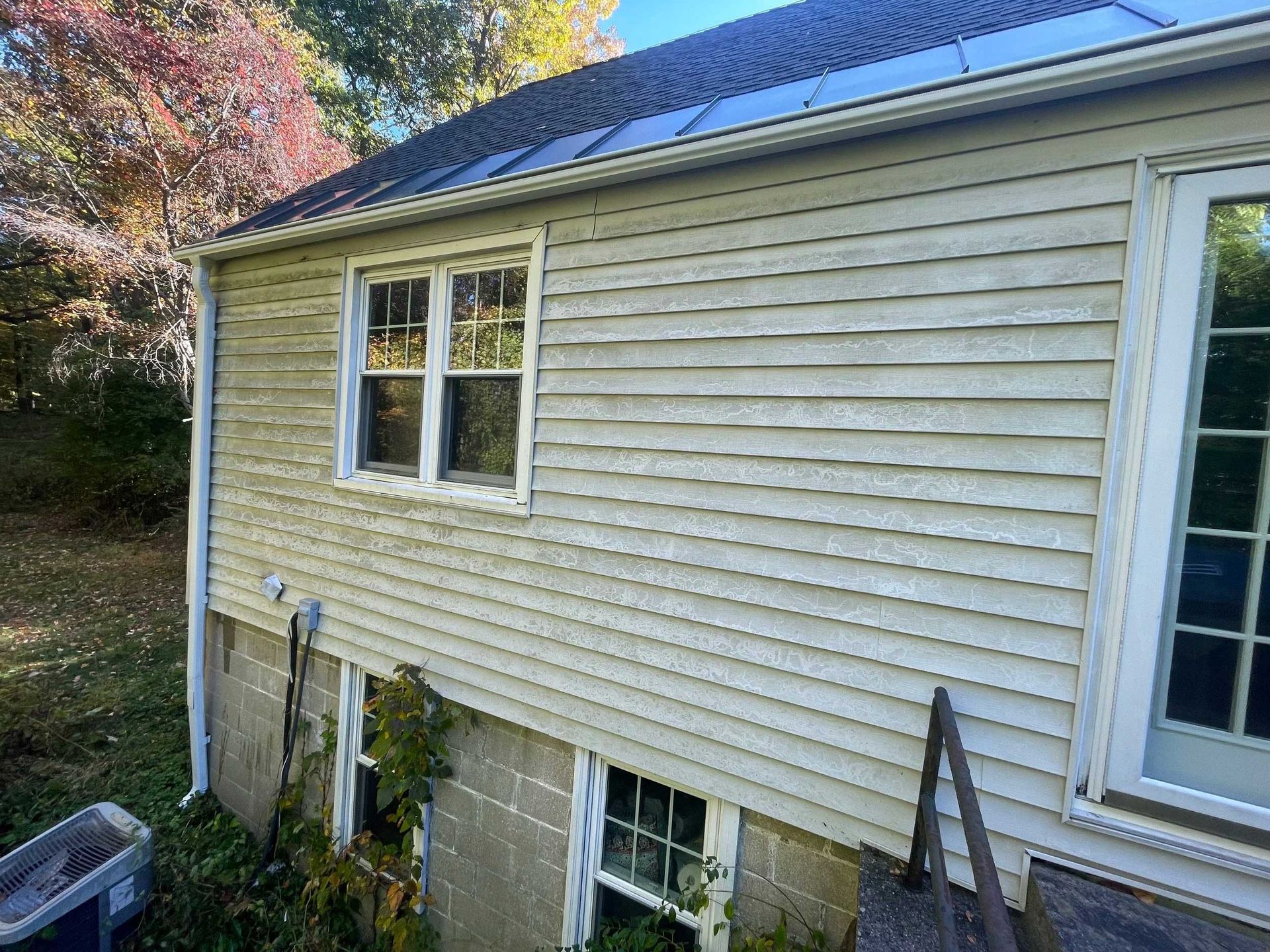 Beige-sided house with a window, white trim, and a concrete foundation. A small gutter runs down the side.
