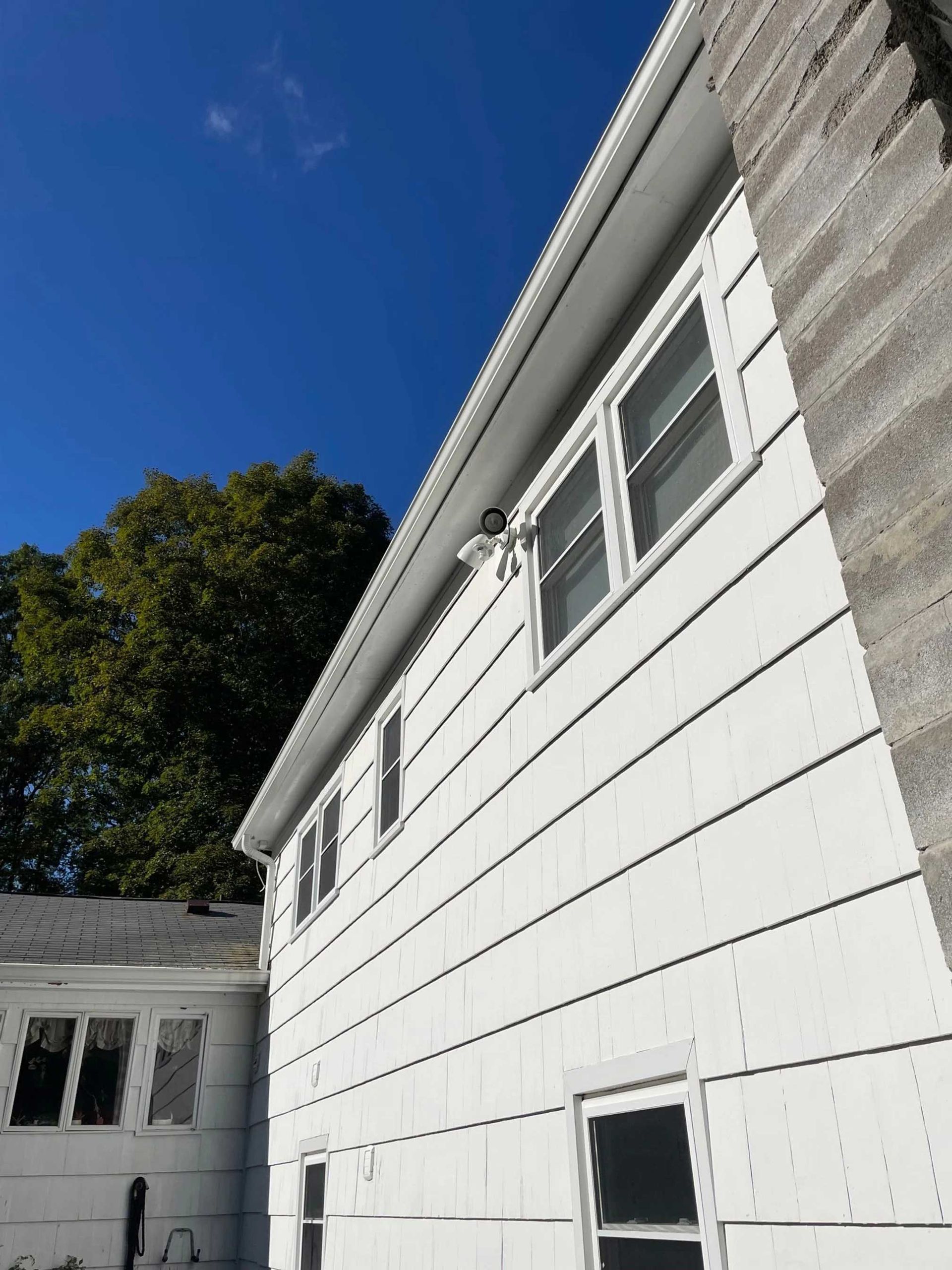 White-sided house with multiple windows and a gray chimney against a blue sky.