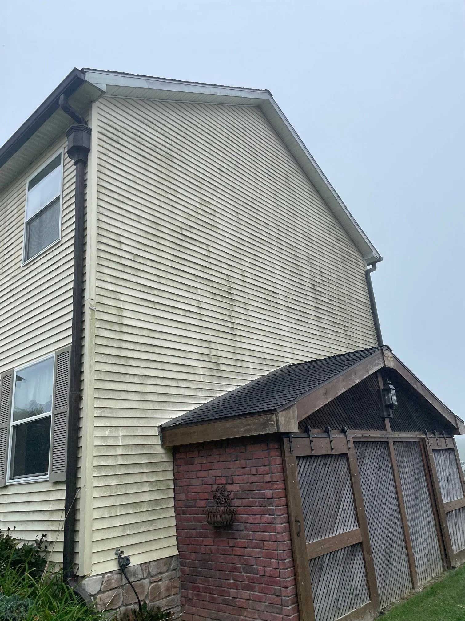 Tan vinyl-sided house with a porch and brick accents; cloudy sky.
