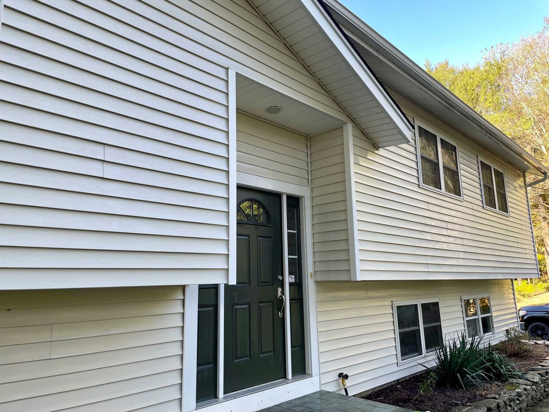 Beige house exterior with dark green door and windows, surrounded by trees.