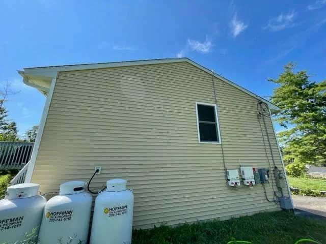 Tan-sided house with propane tanks below. Blue sky above. One window.
