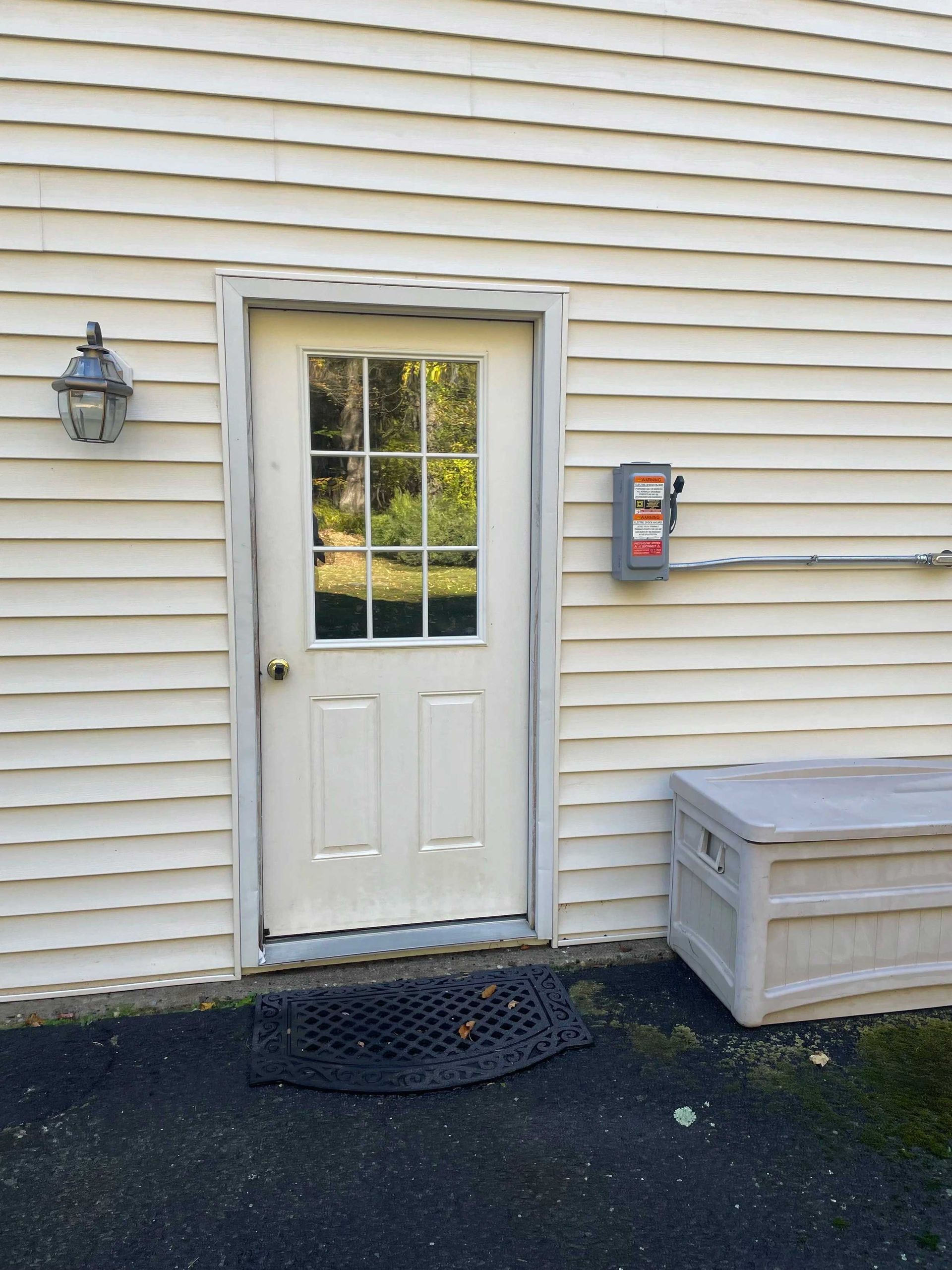 White door with glass panel, exterior wall, lantern, electrical box, and storage chest.