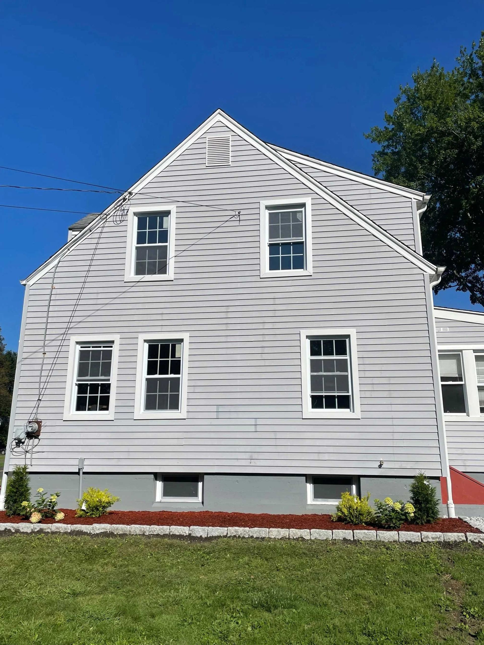 Gray house with white-framed windows against a blue sky, with a lawn in the foreground.