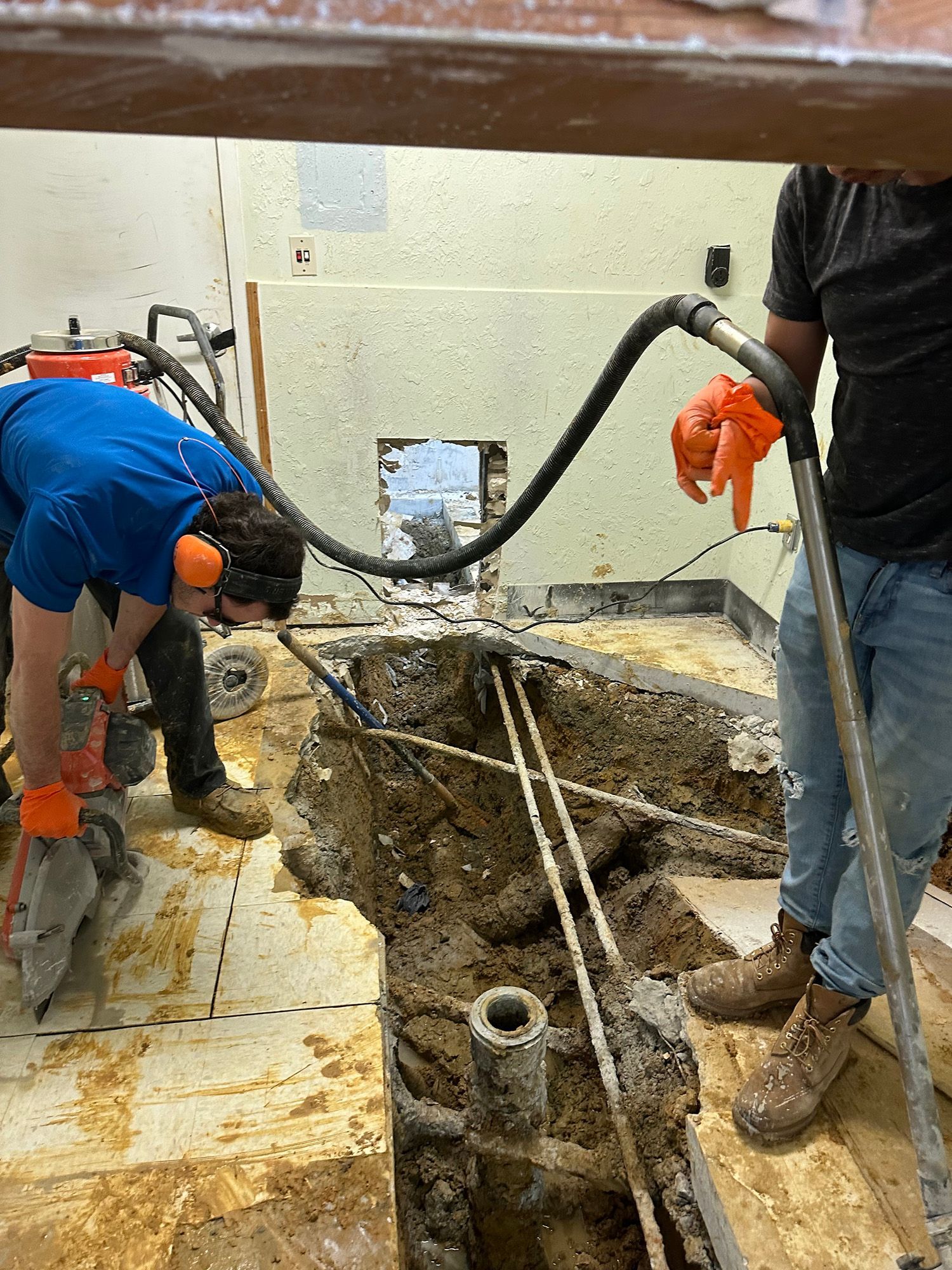 Two workers in a construction site, breaking concrete. One uses a jackhammer, the other holds a hose.