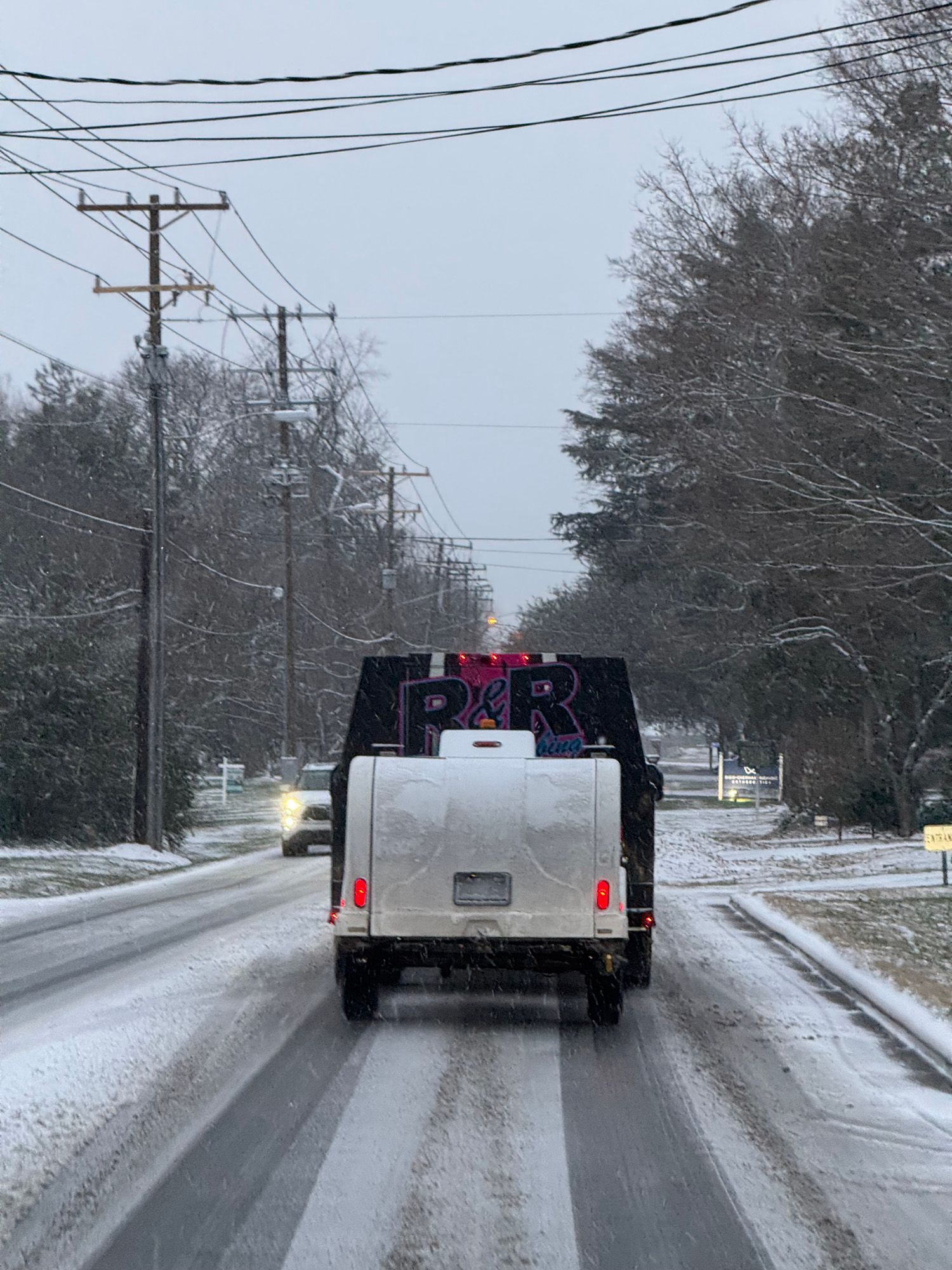 Truck driving on a snow-covered road, trees and power lines in the background. Winter weather.