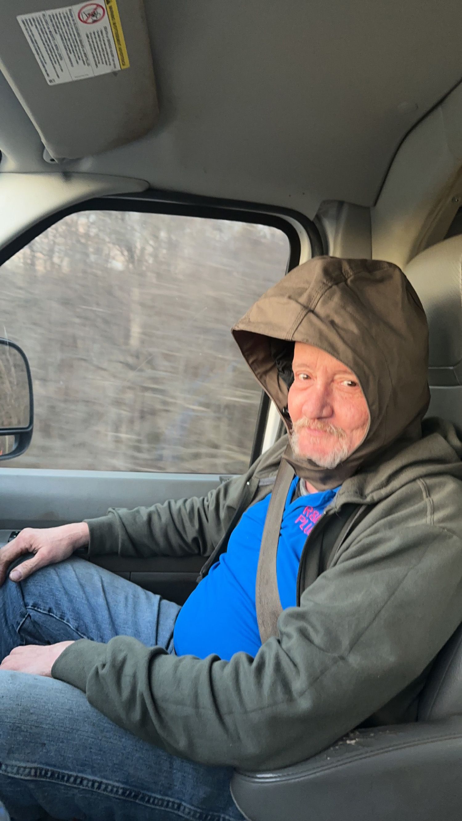 Man in a hooded jacket inside a vehicle, smiling.