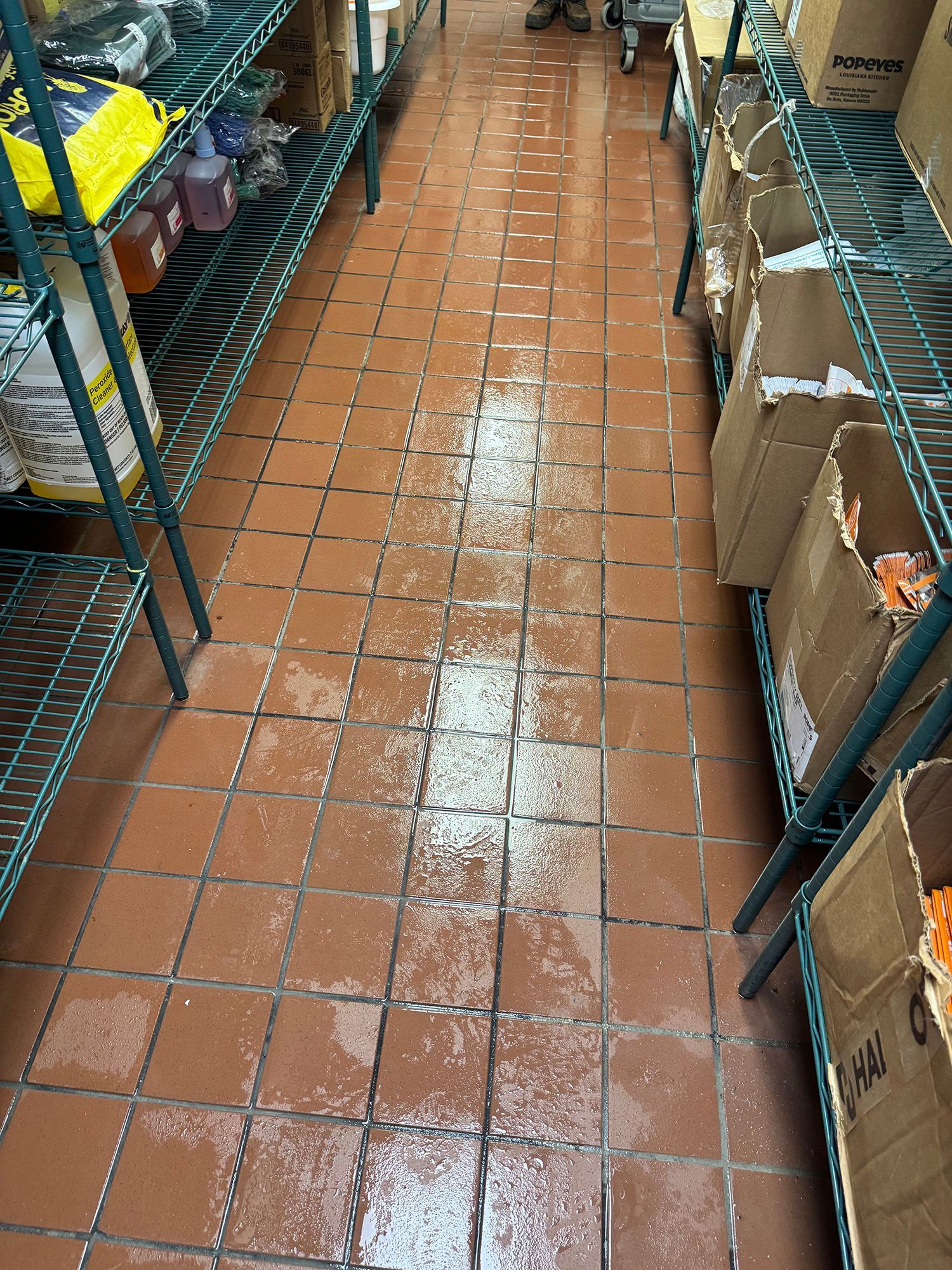 Wet, tiled floor in a storage room with shelving.