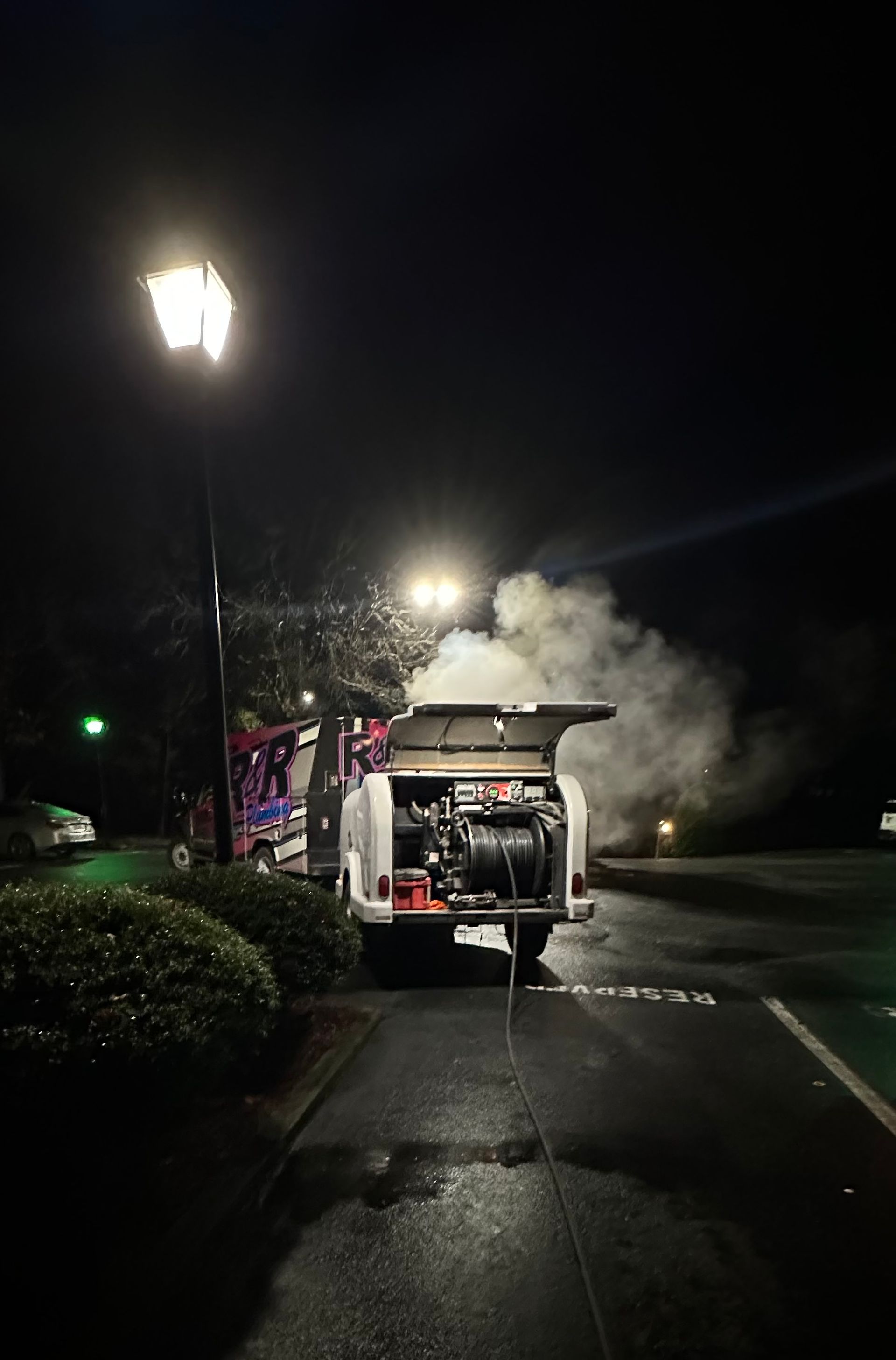 A white utility vehicle with smoke billowing out in a dark parking lot at night.