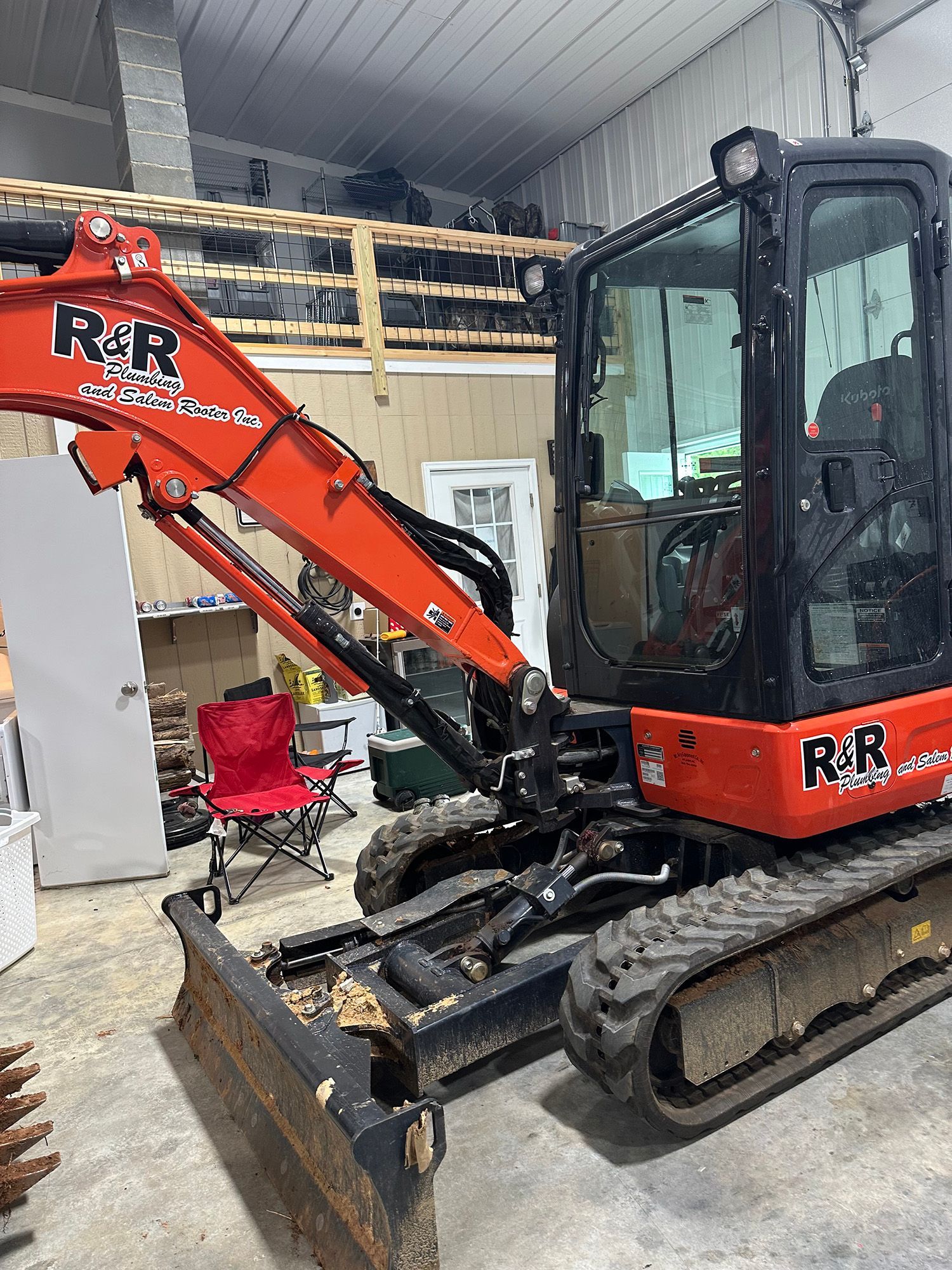 Orange and black R&R mini excavator inside a garage.