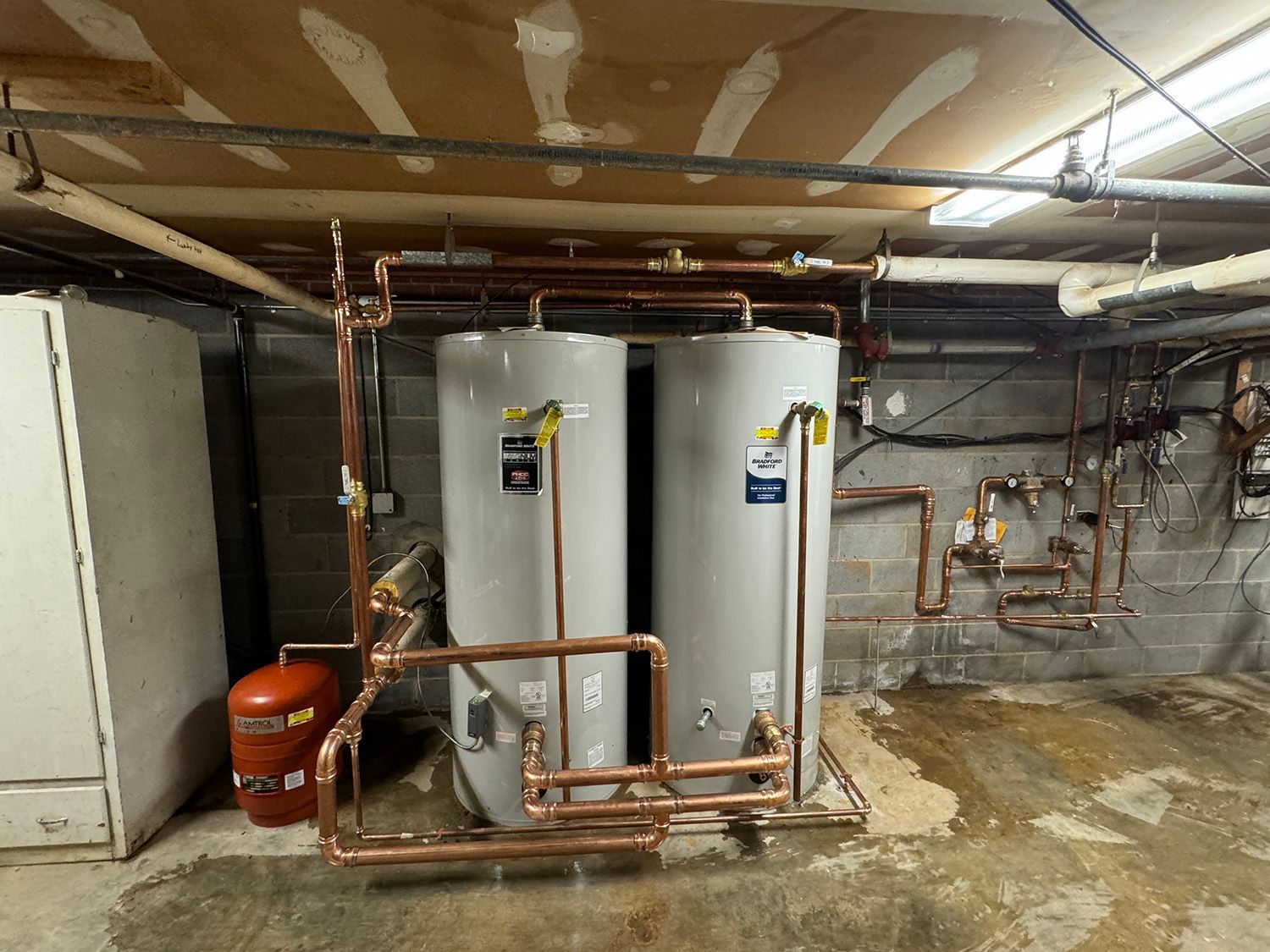 Two water heaters with copper pipes in a basement.