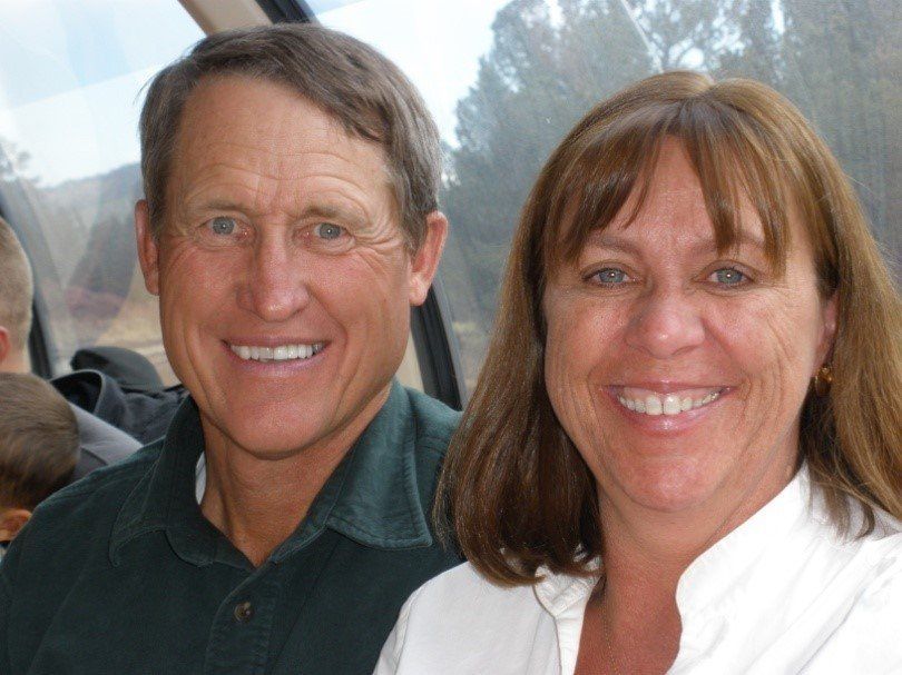 Two smiling people sitting close together, wearing dark and white tops, outdoors at an event.