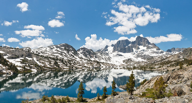 Snowy mountain peaks above a turquoise alpine lake under a bright blue sky with clouds