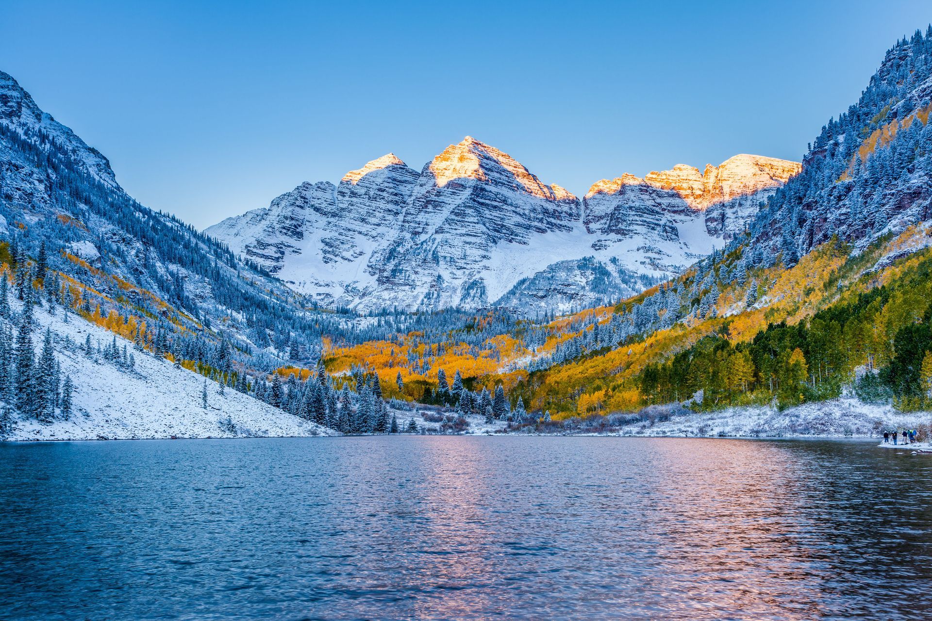 Snowy mountain peaks and autumn-colored trees reflected in a calm alpine lake