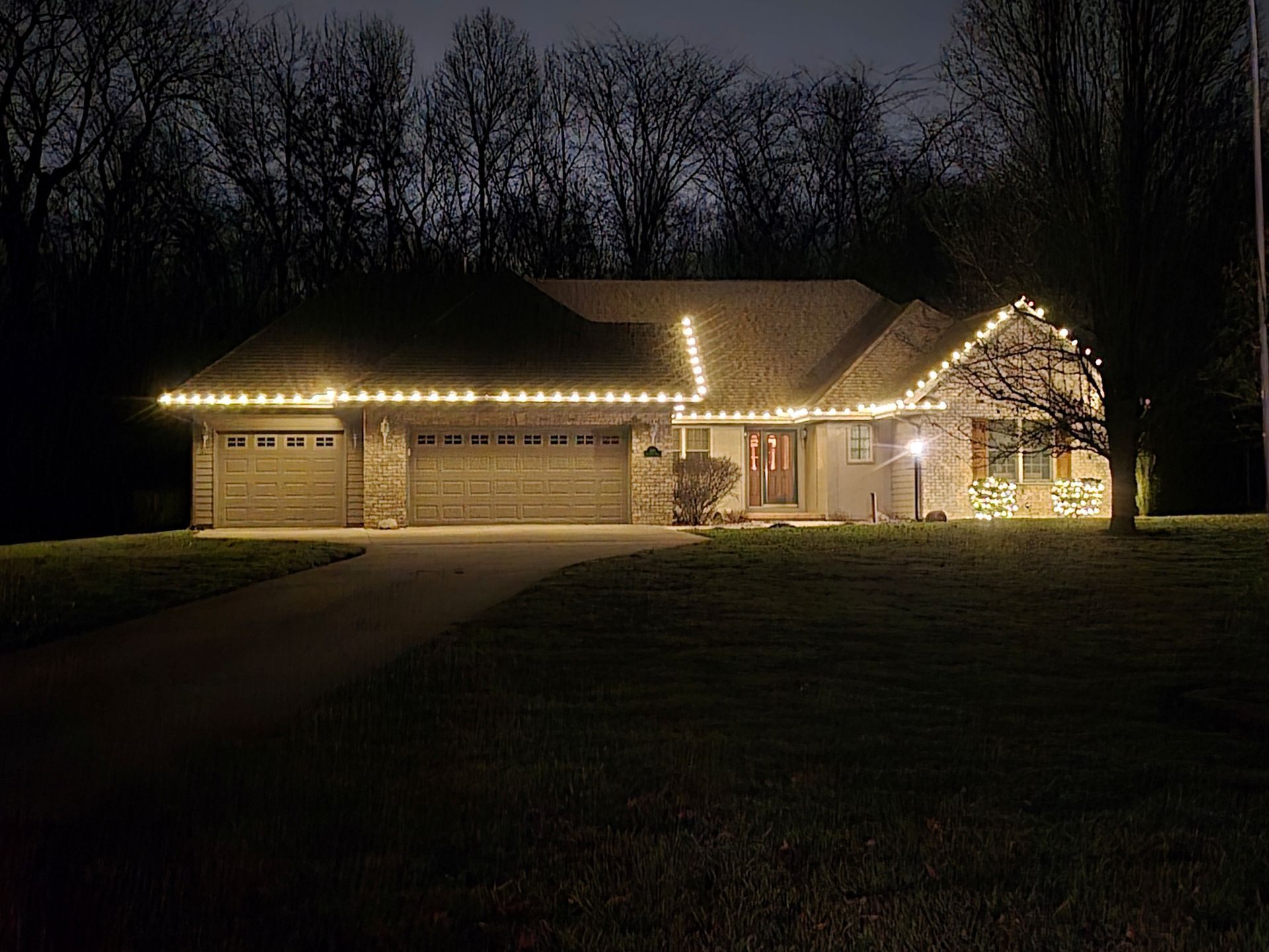 House at night decorated with white lights along the roof and ground.