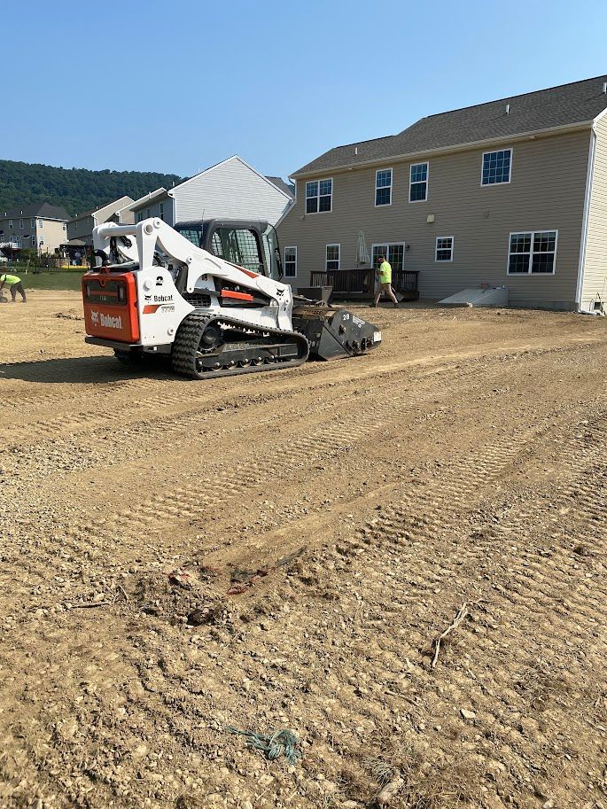 A bobcat is sitting in a dirt field in front of a house.