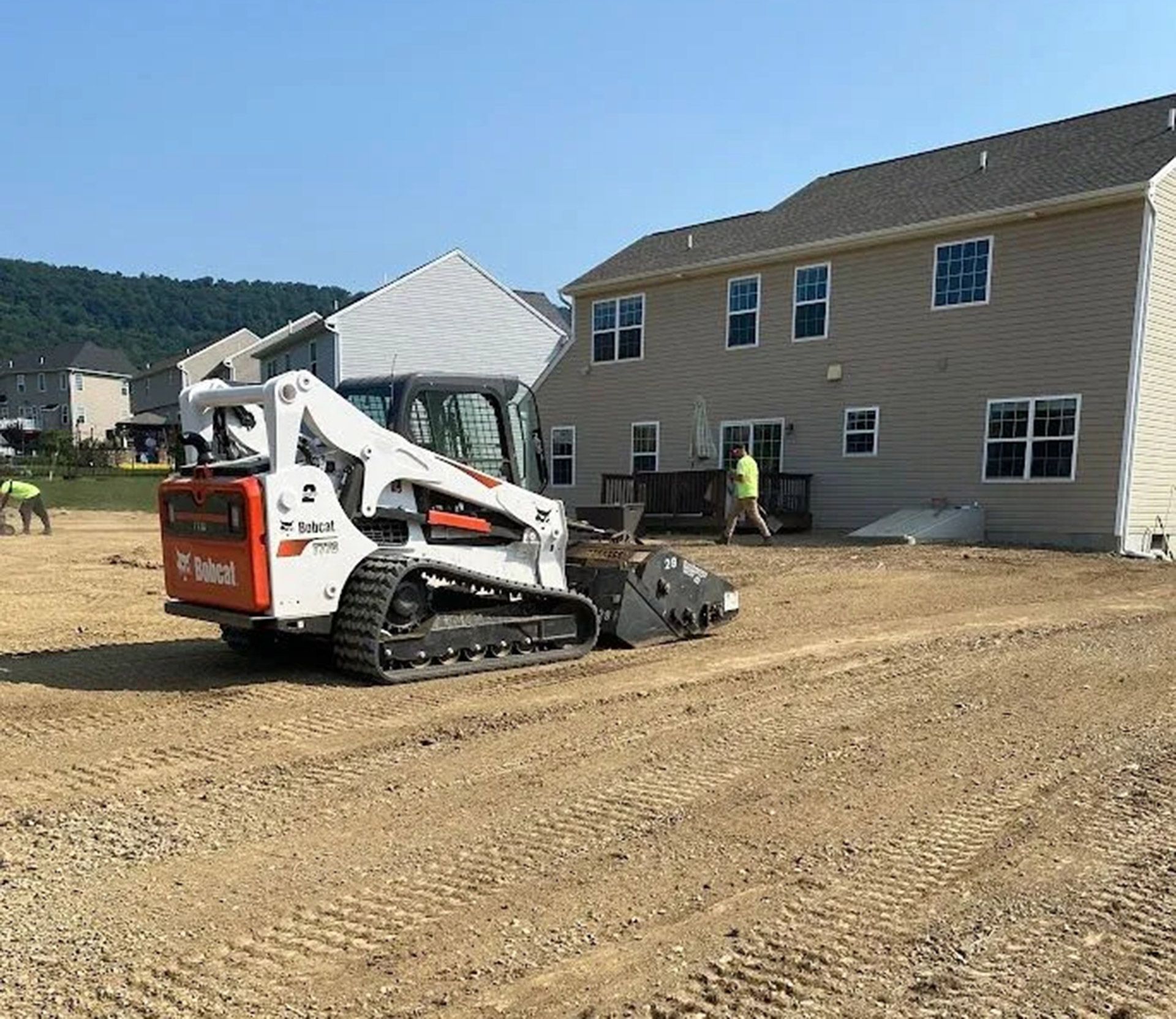 A bobcat is moving dirt in front of a house