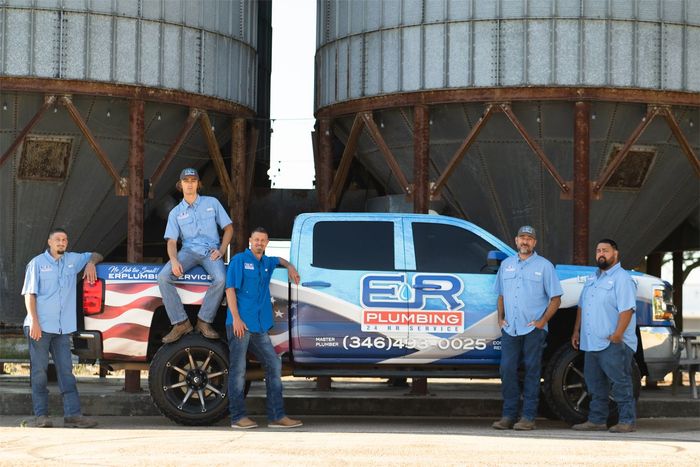 Five men pose beside a blue work truck in front of large industrial silos.