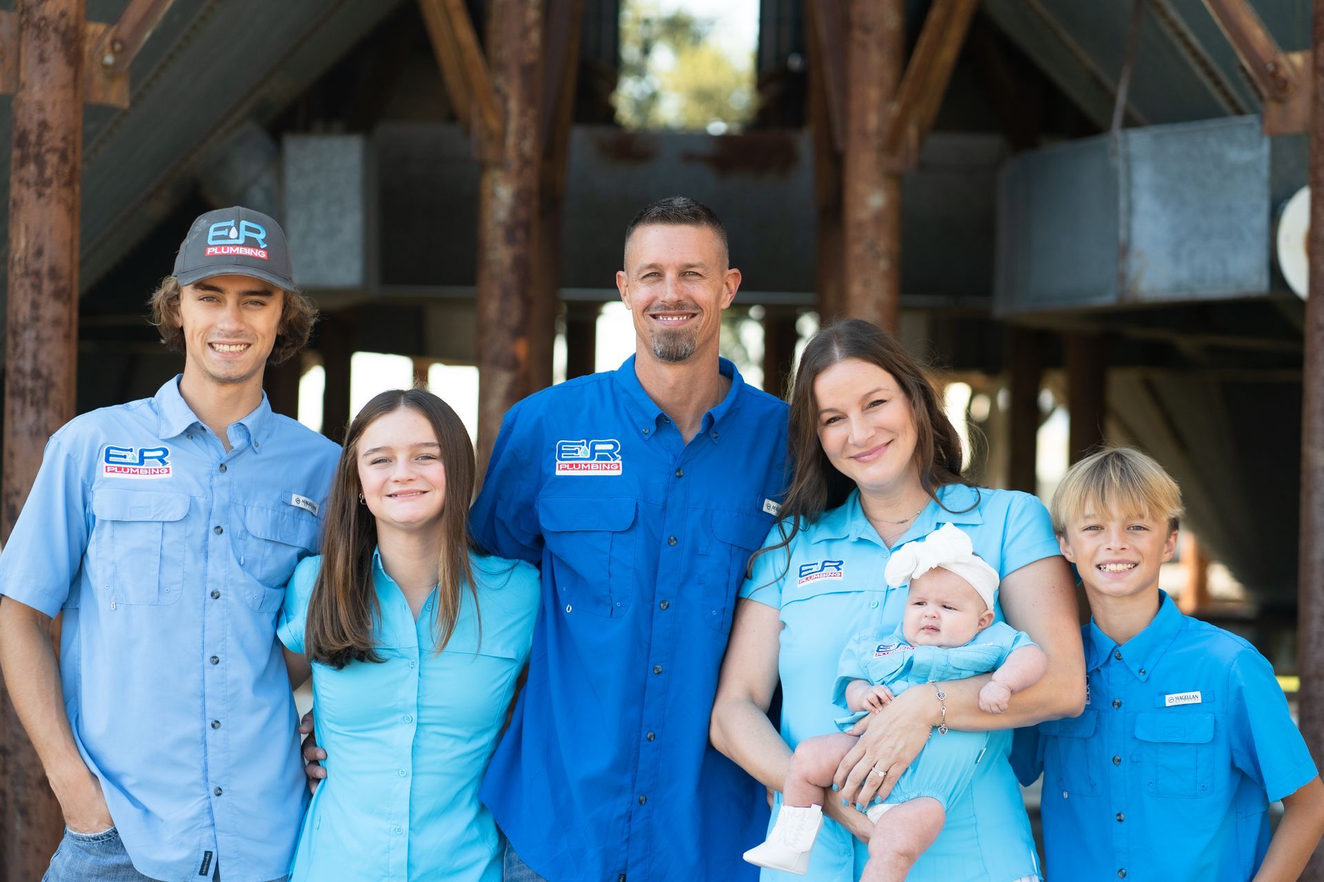 Family of six in blue shirts, posing in front of a weathered structure.