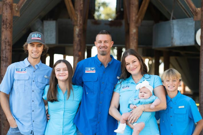 Family of six in blue shirts, posing in front of a weathered structure.