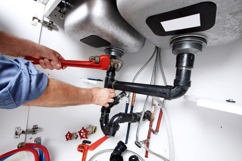 A plumber is fixing a sink with a wrench.