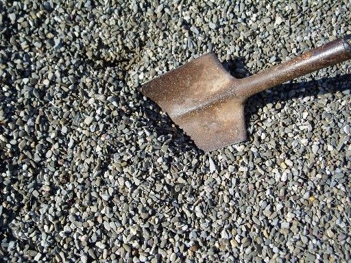 Shovel resting on a bed of gravel, with dark gray stones.