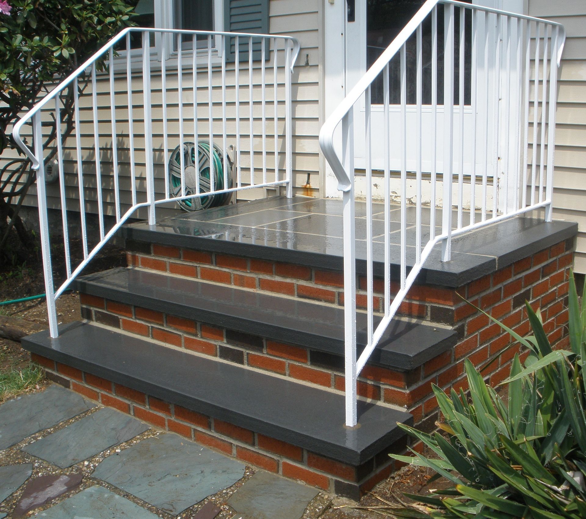 Brick steps leading to a house, with a white railing.