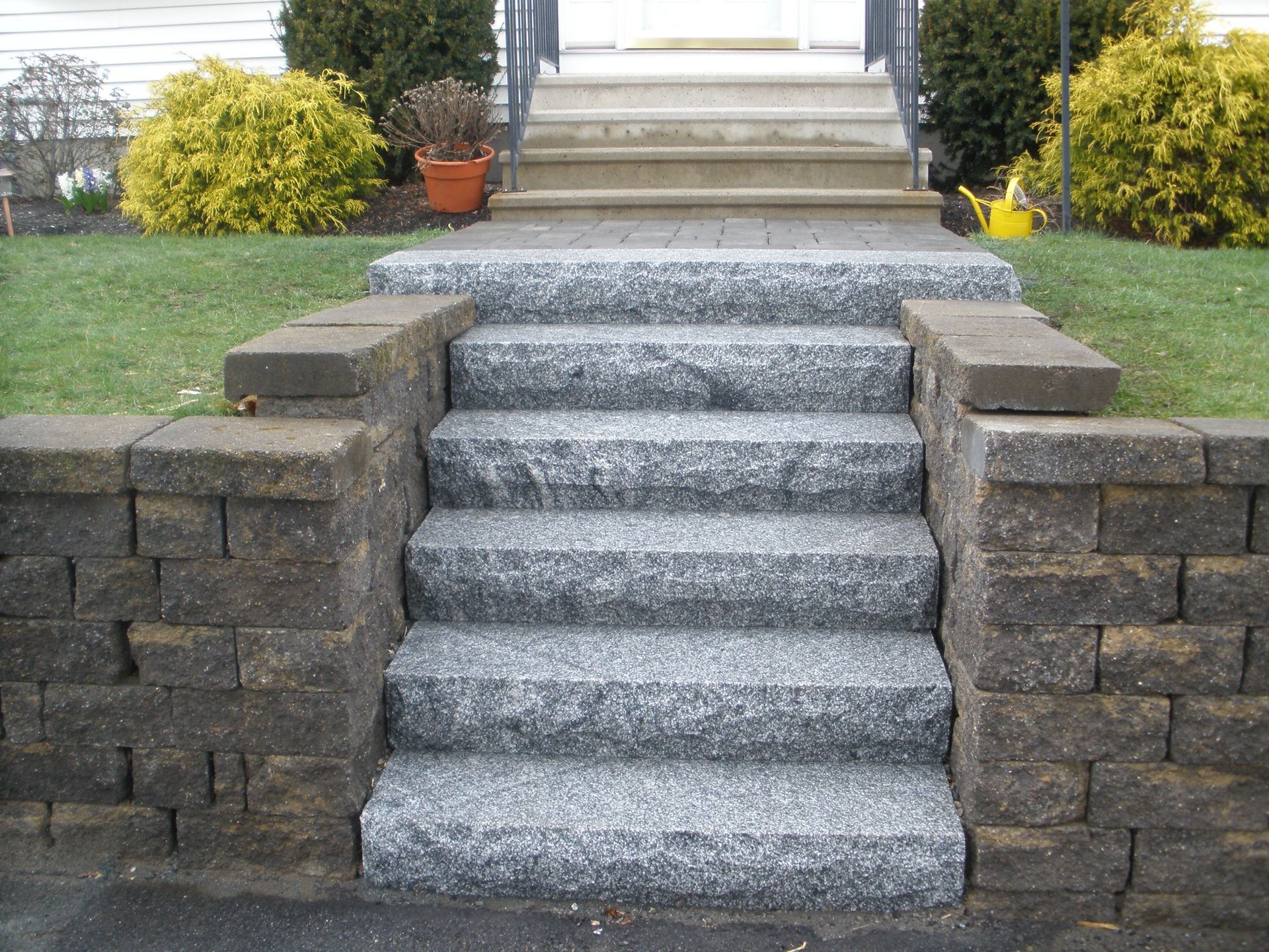 Stone steps leading to a house entrance, flanked by retaining walls and landscaping.