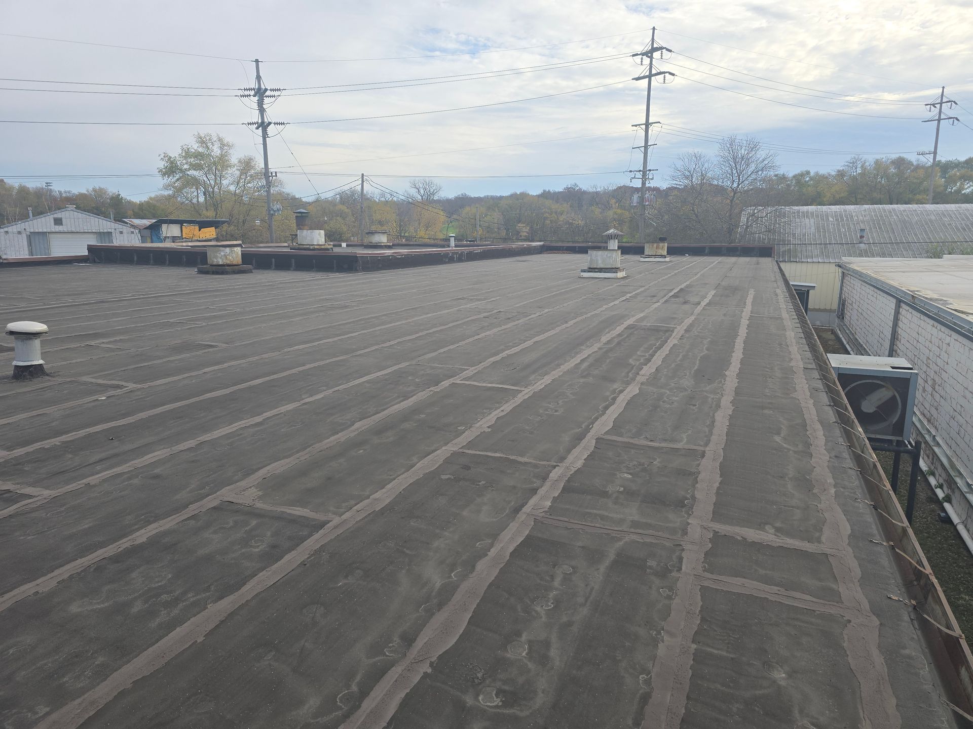 Flat, black industrial roof with raised seams; power lines in the background.