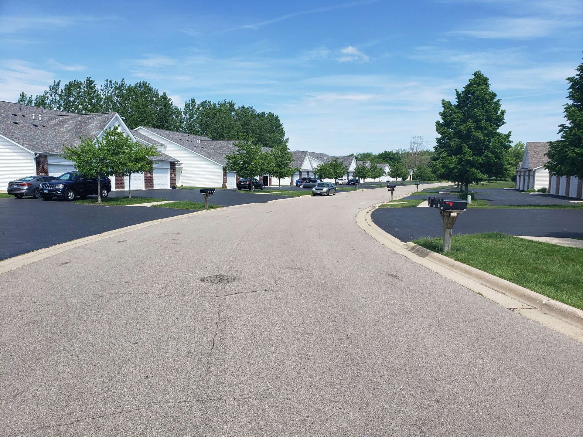 A quiet residential street with houses, trees, and parked cars on a sunny day.