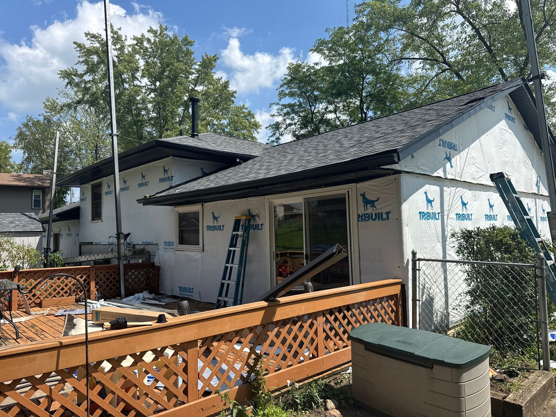 House exterior under construction; white siding with blue wrap, wooden deck.