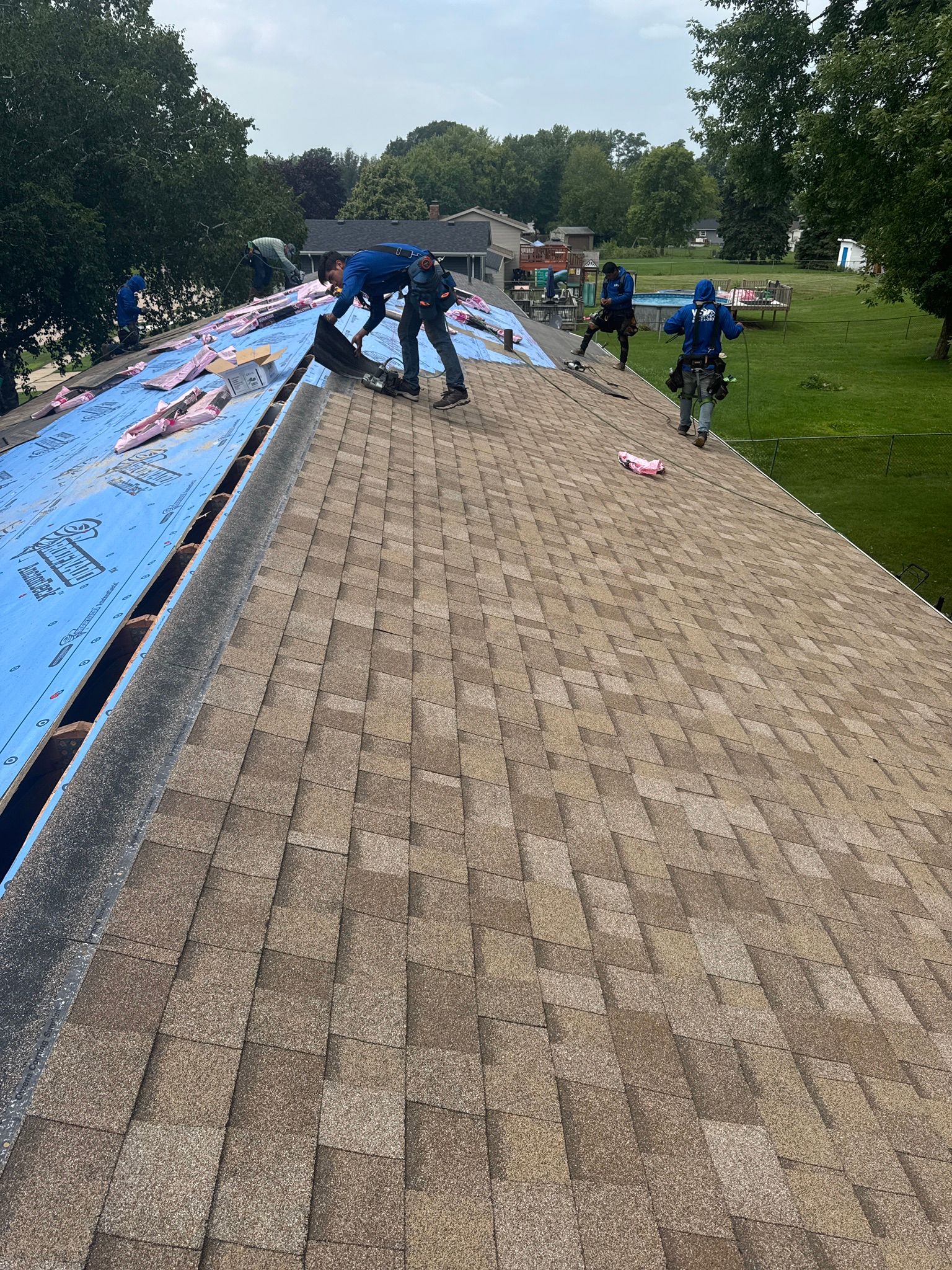 Roofers in blue shirts install roofing material on a sloped roof.