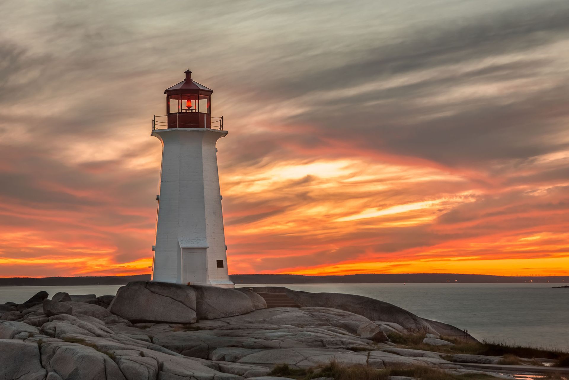 A lighthouse is sitting on top of a rocky cliff overlooking the ocean at sunset.