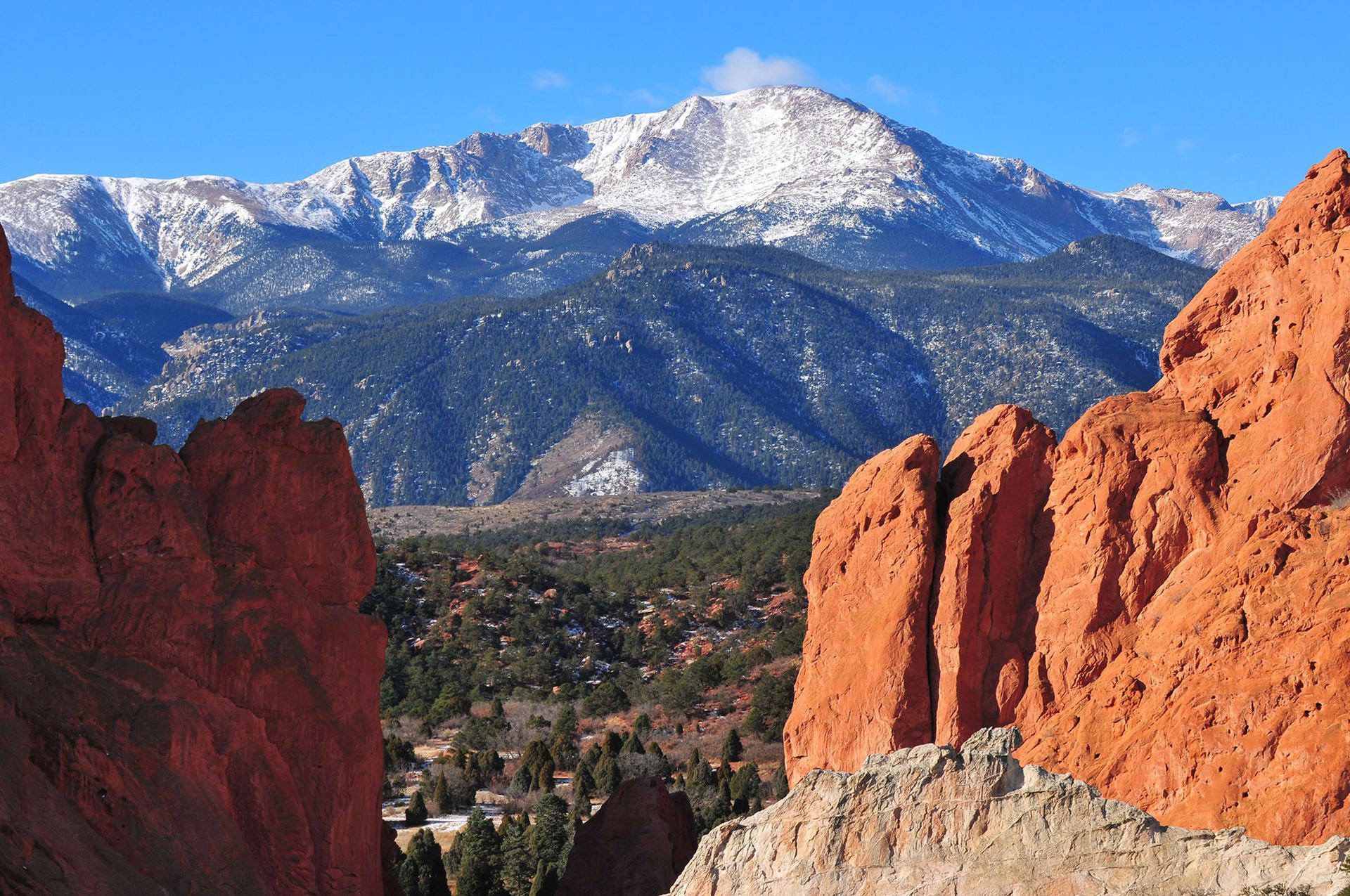 A mountain with snow on it is surrounded by rocks and trees.