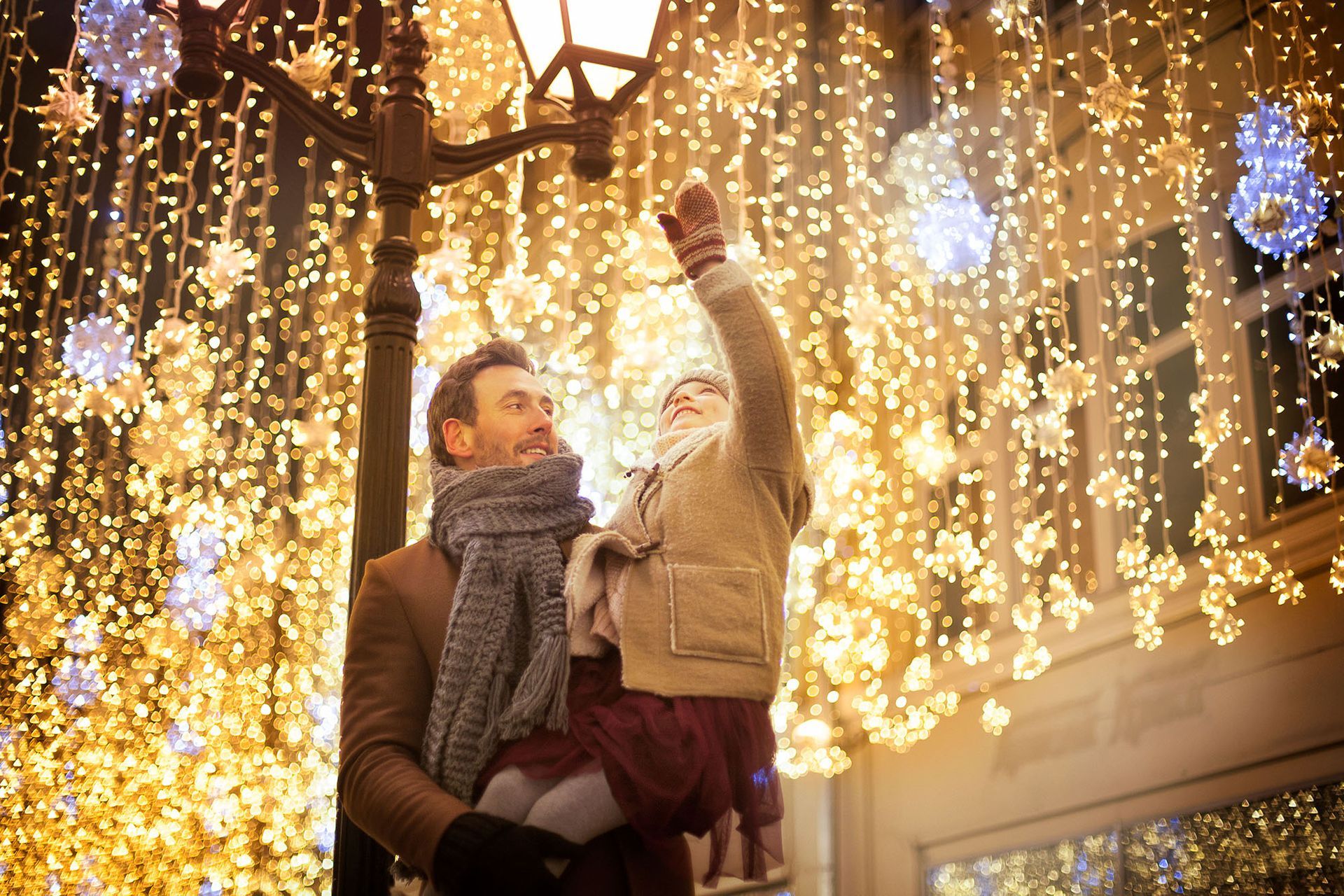 A man carrying his child are looking at Christmas lights on a street.