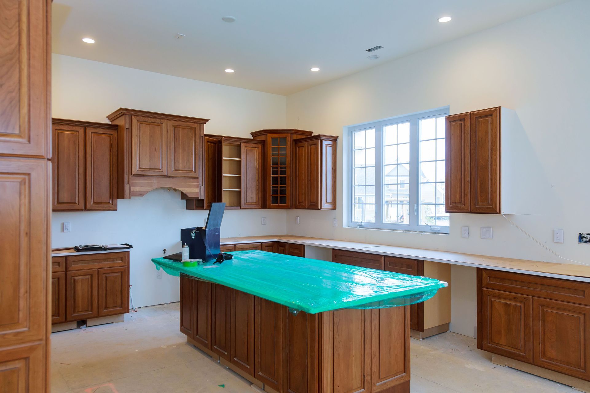 Empty kitchen with wooden cabinets, a center island, and a large window letting in daylight.
