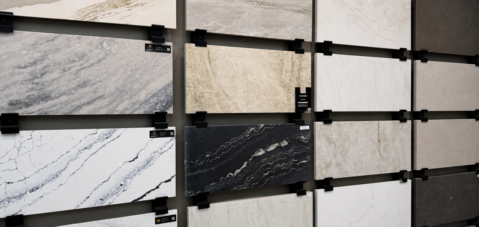 Display of textured stone tile samples in white, beige, gray, and black on a wall rack