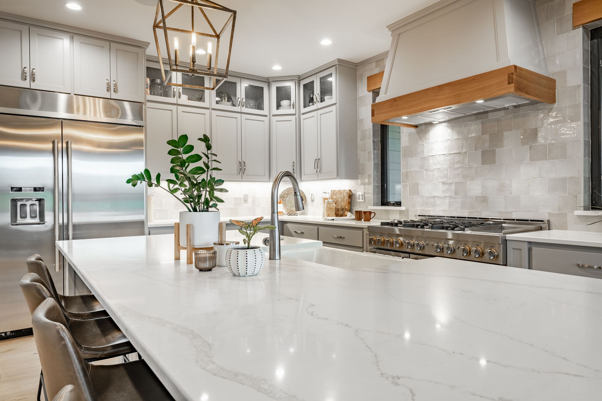 Modern white kitchen with large island, stainless steel appliances, pendant lights, and wood range hood