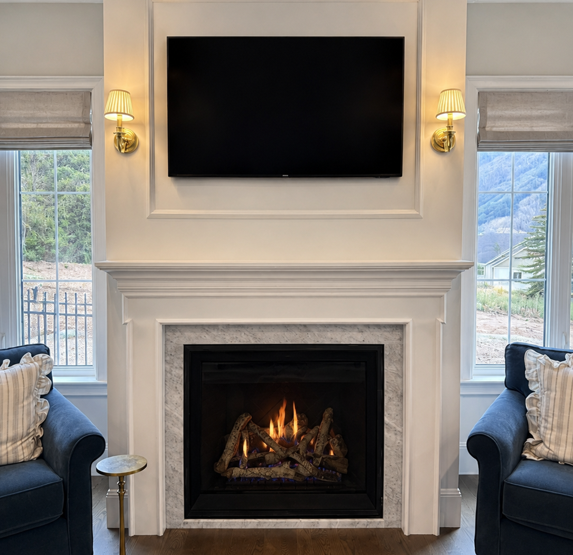 Elegant living room with a wall-mounted TV above a lit fireplace between two windows and blue chairs