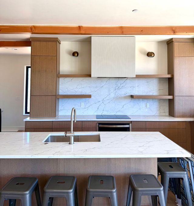 Modern kitchen with white marble island, wood cabinets, open shelves, and stainless range hood
