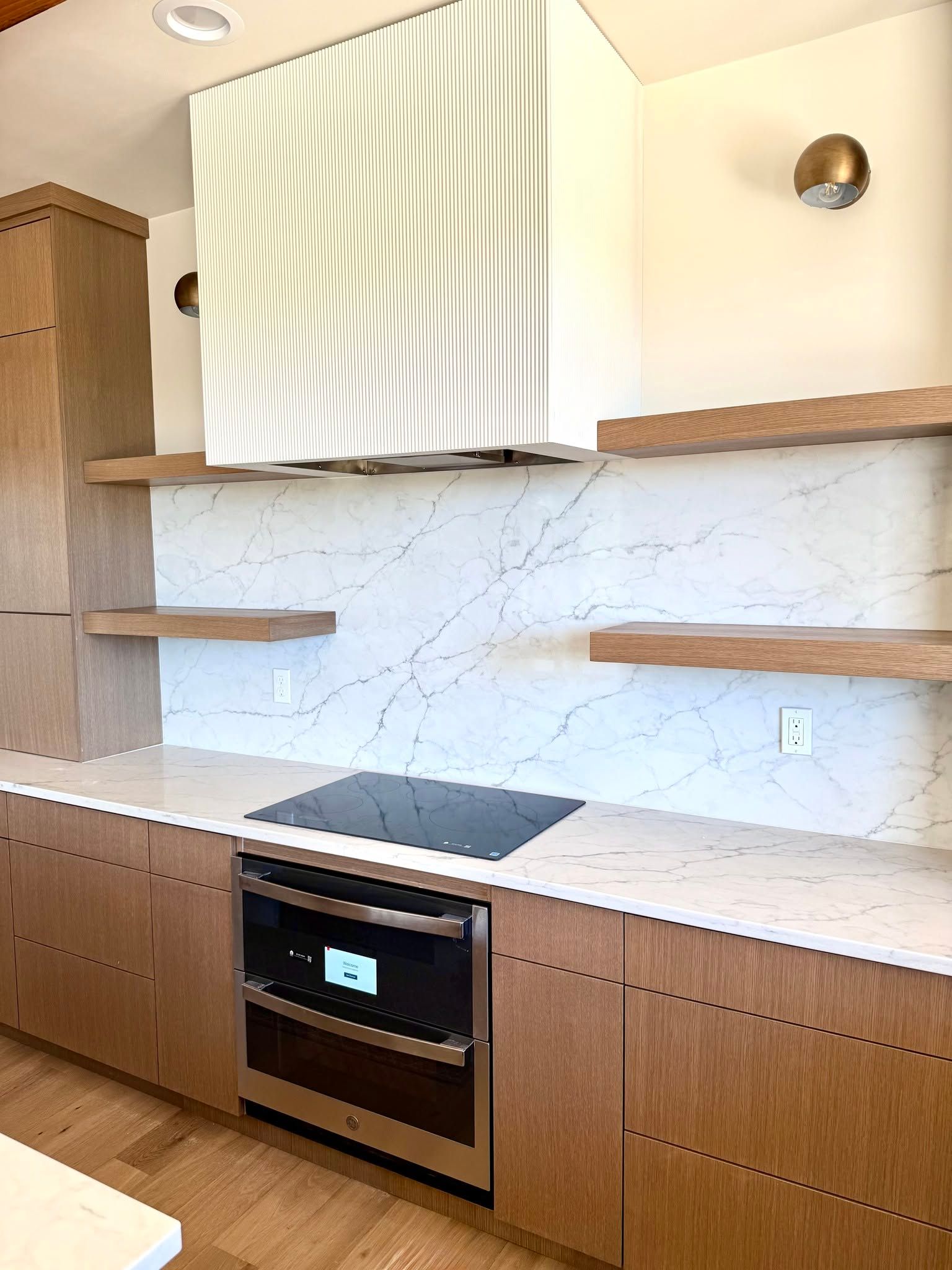Modern kitchen with wood cabinets, marble-look backsplash, open shelves, and built-in oven