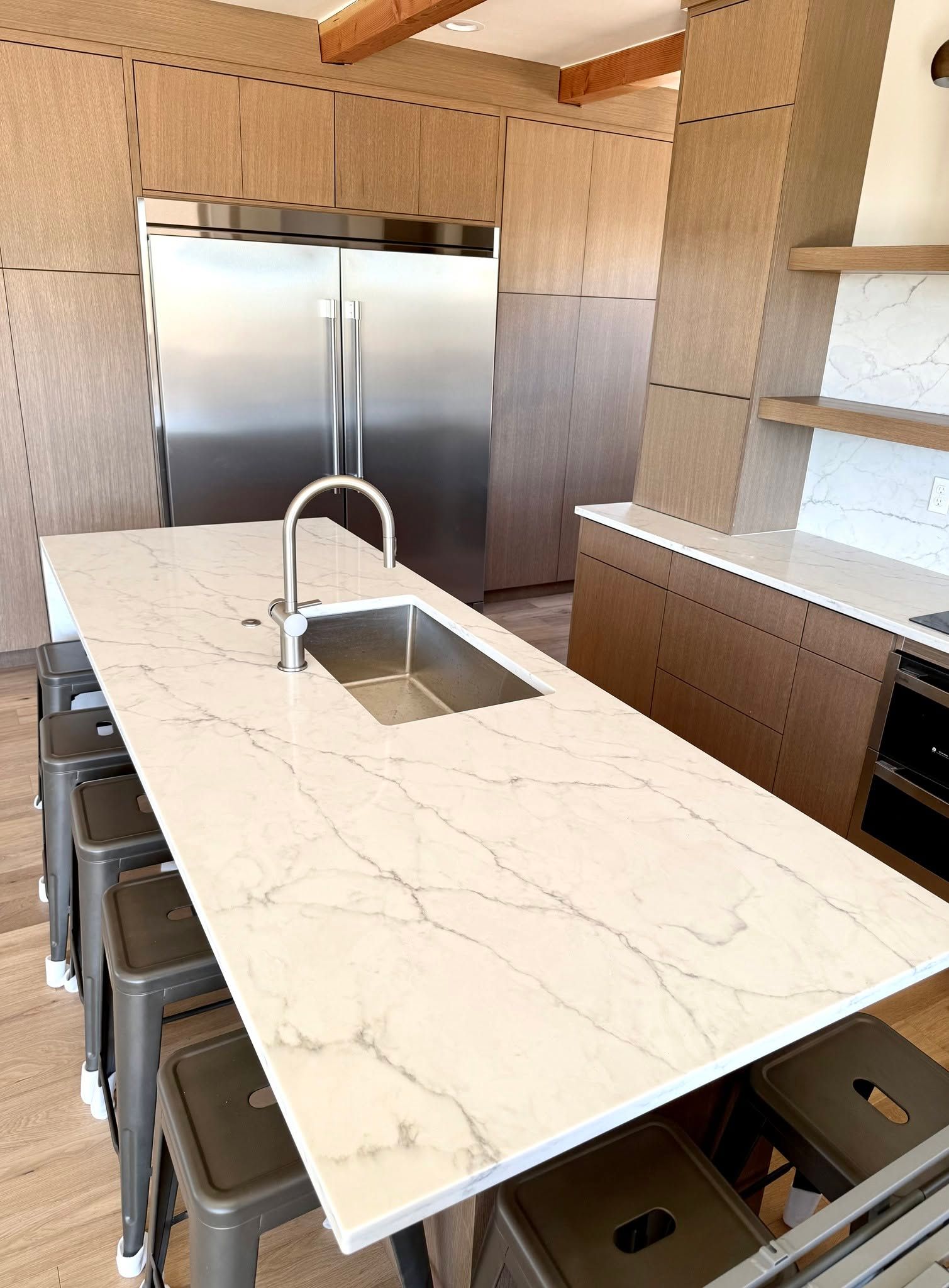 Modern kitchen with marble island, sink, bar stools, and stainless steel refrigerator