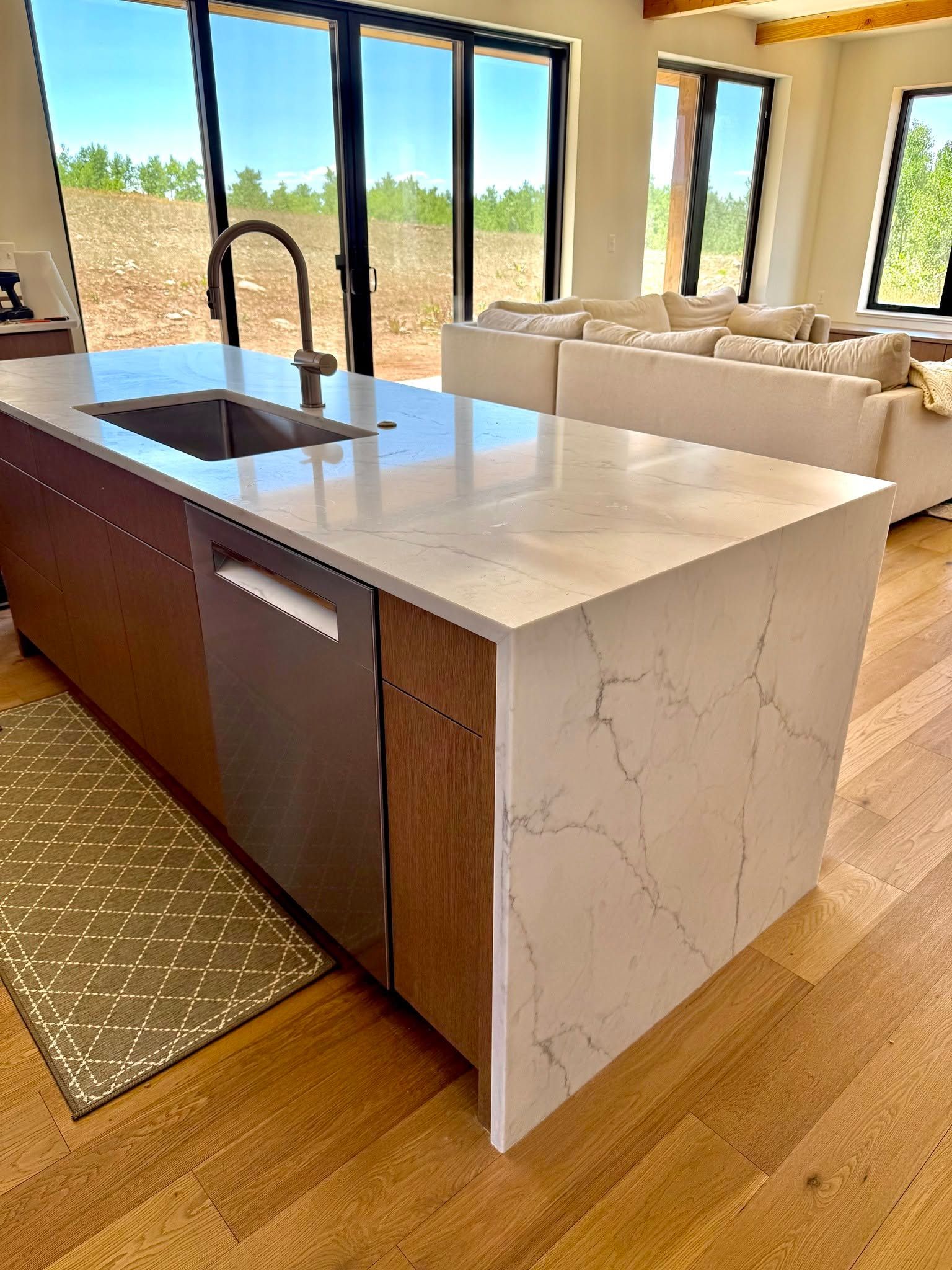 Modern kitchen with marble island, dark faucet, and large windows overlooking a bright living area